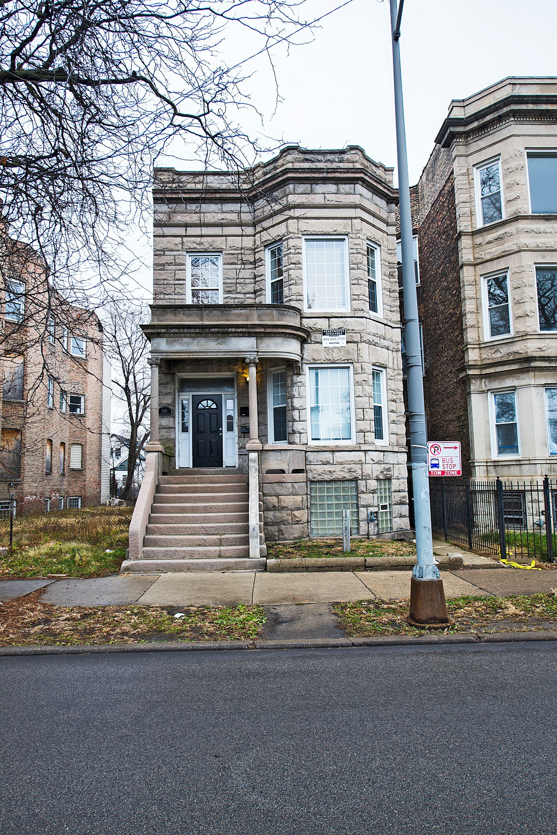 Stone facade building with stairs and a door. Another building on either side. Gloomy sky.