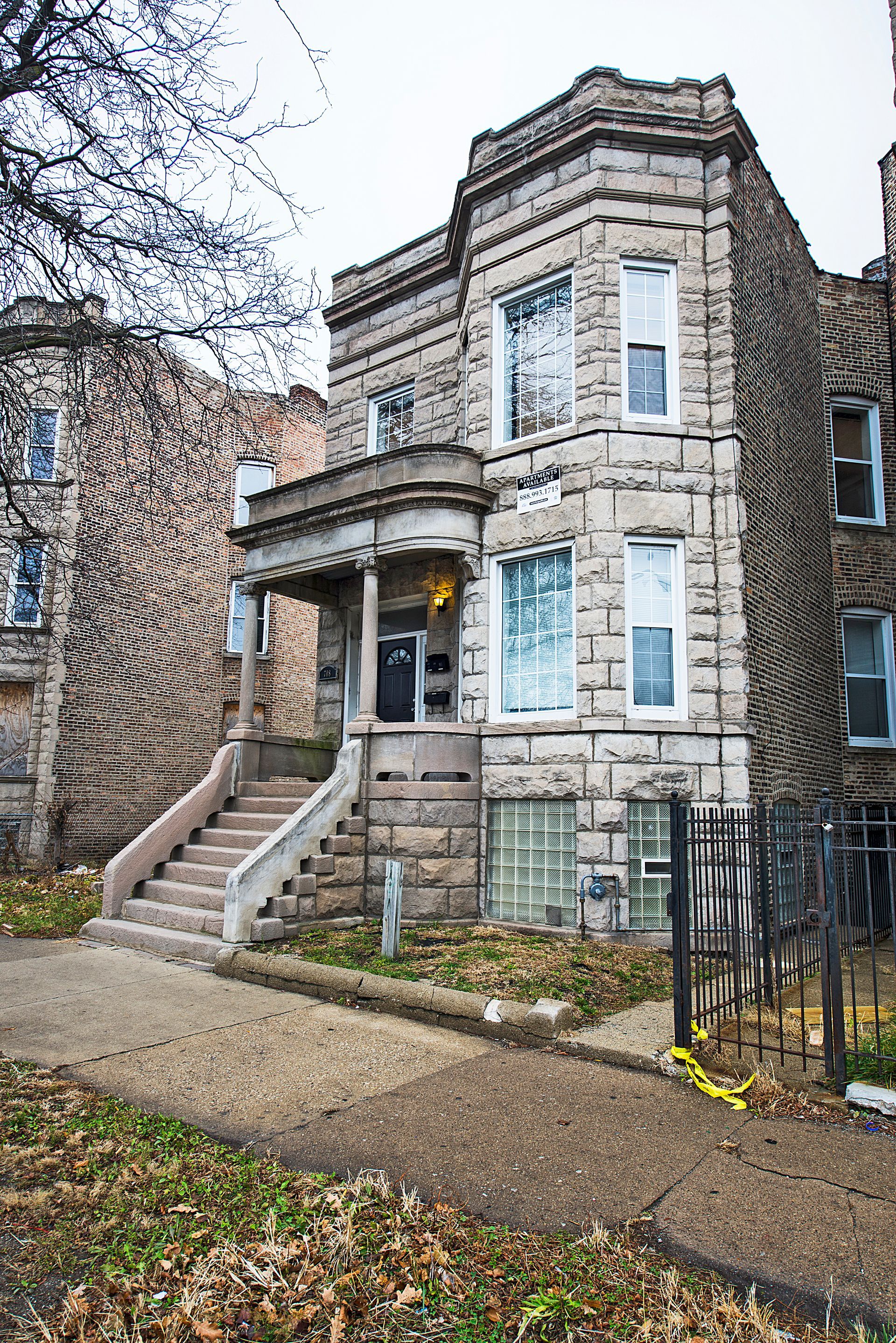 Three-story stone building with a porch and steps, on a city street.