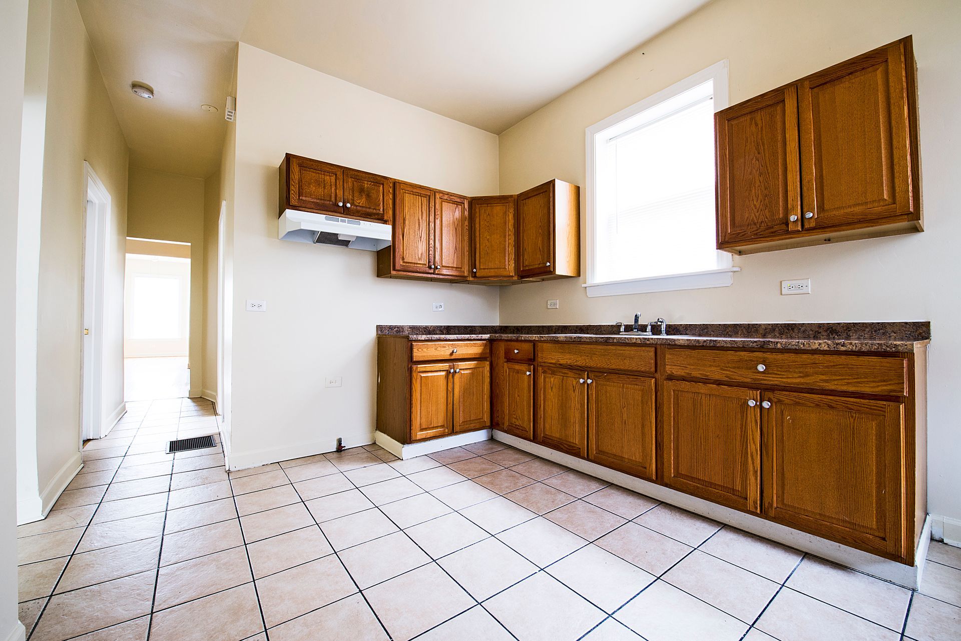 Empty kitchen with brown cabinets, light countertops, and white tile floor.