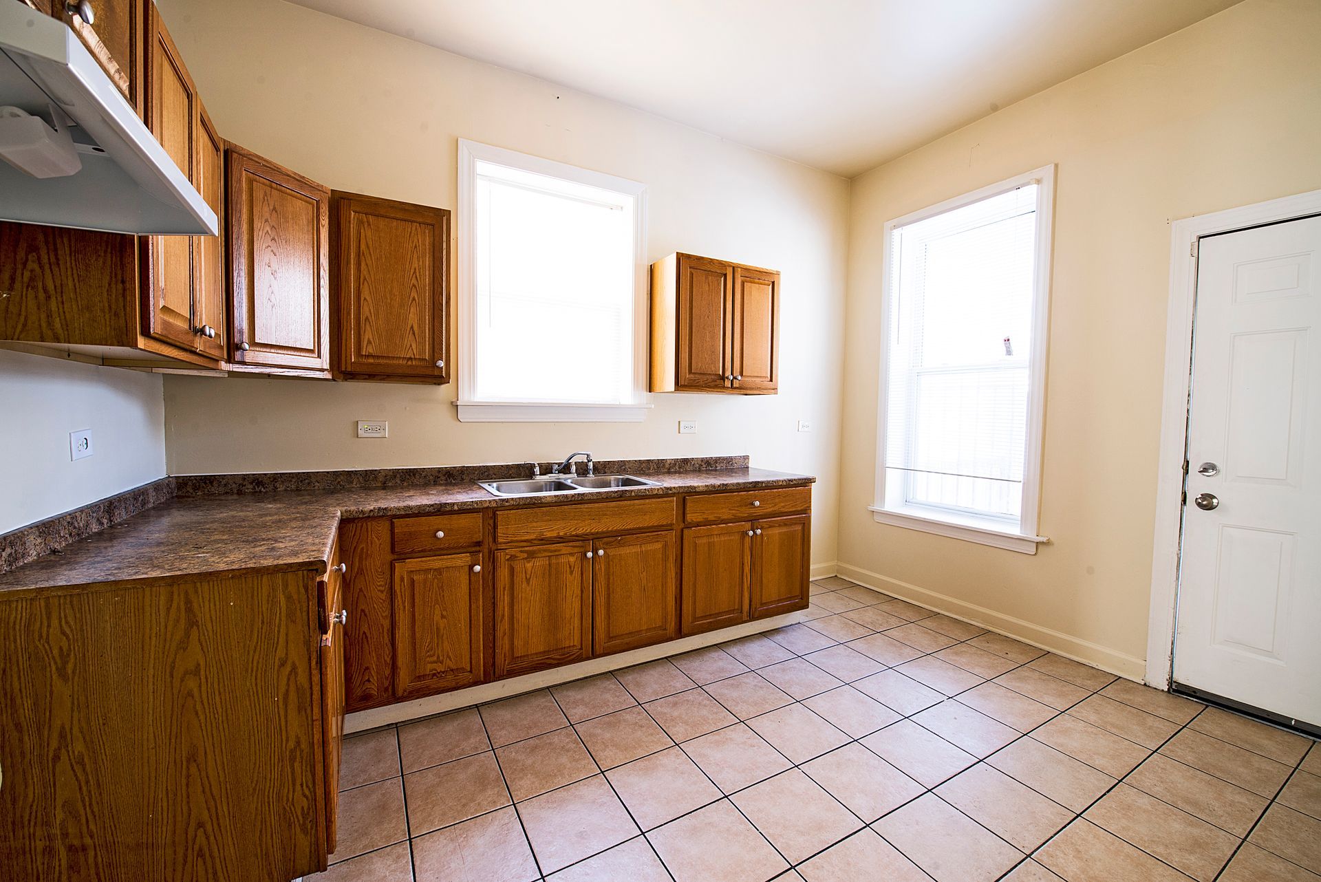 Empty kitchen with wooden cabinets, beige walls, and tiled floor.