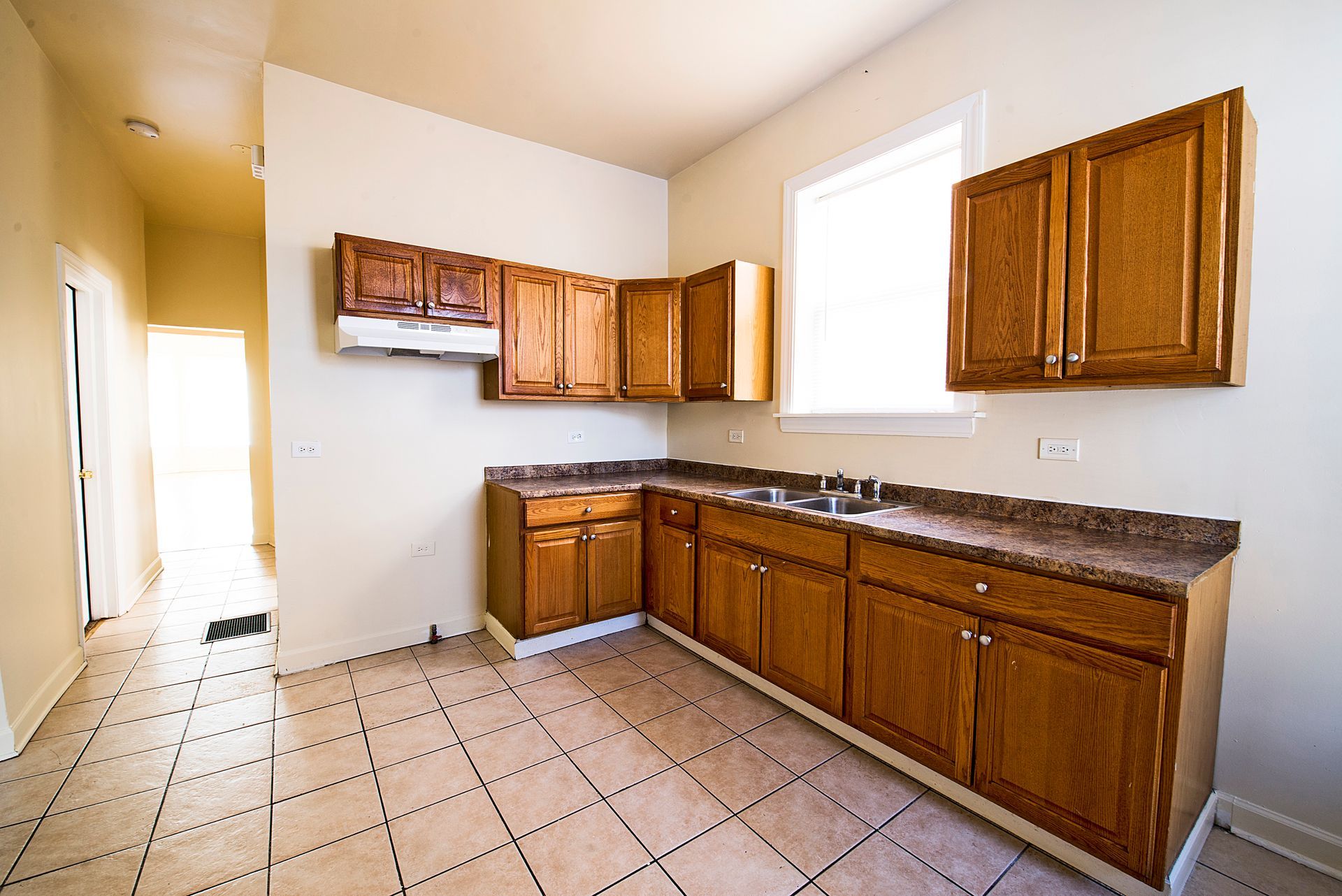 Empty kitchen with wooden cabinets, countertop, and tiled floor. A doorway is visible.