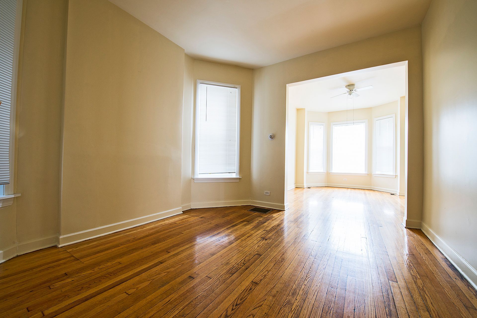 Empty room with hardwood floors, beige walls, and three windows.