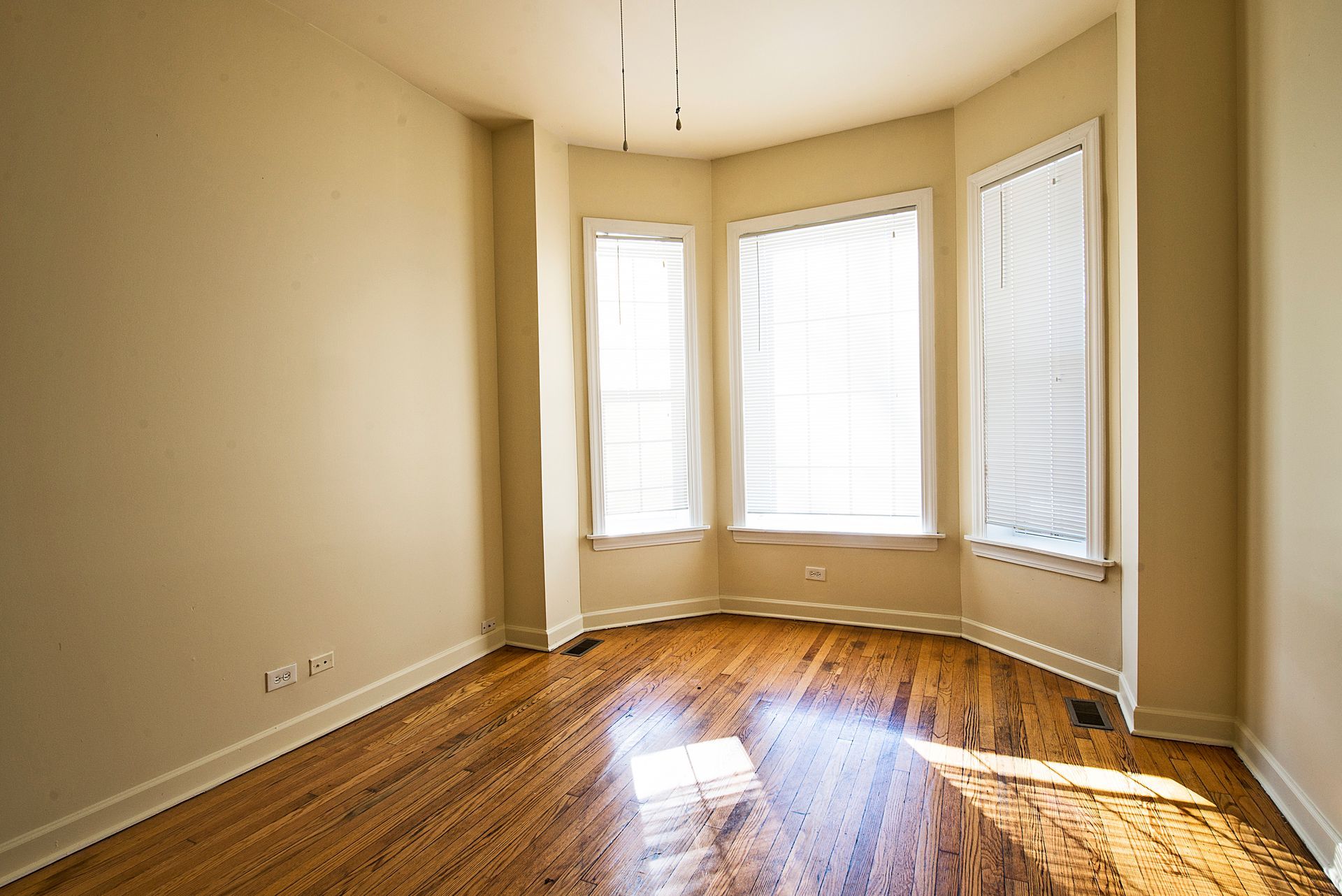 Empty room with wooden floors, bay window with blinds.