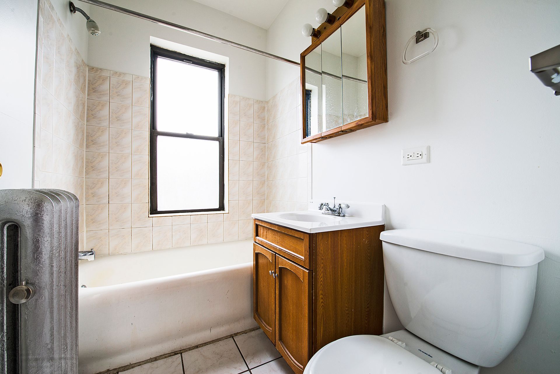 Bathroom with a white toilet, brown vanity, bathtub, window, and tiles.