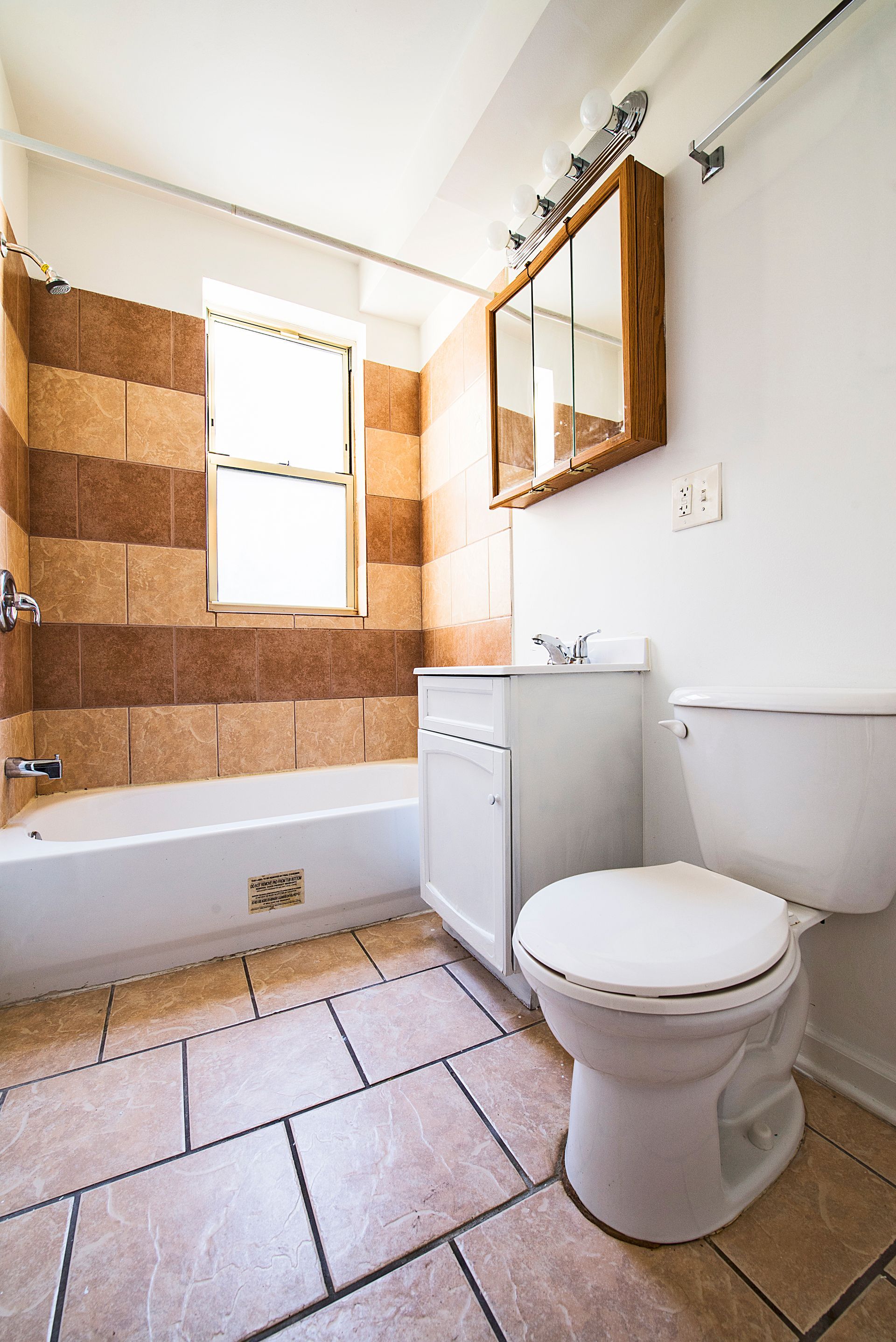 Bathroom with a bathtub, toilet, sink, mirror, and tiled floor and walls.