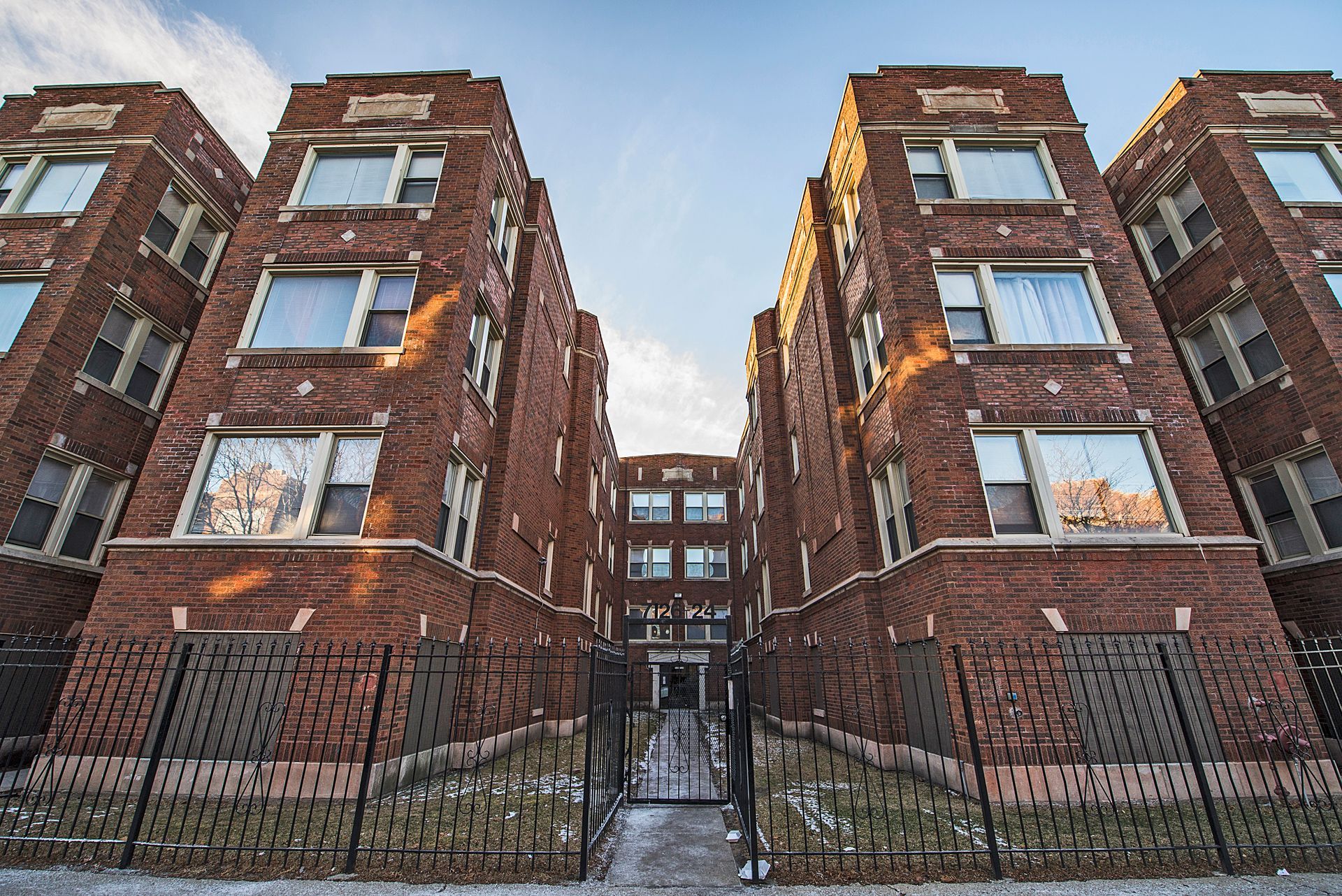 Brick apartment buildings with a gated entrance and a sunny sky.
