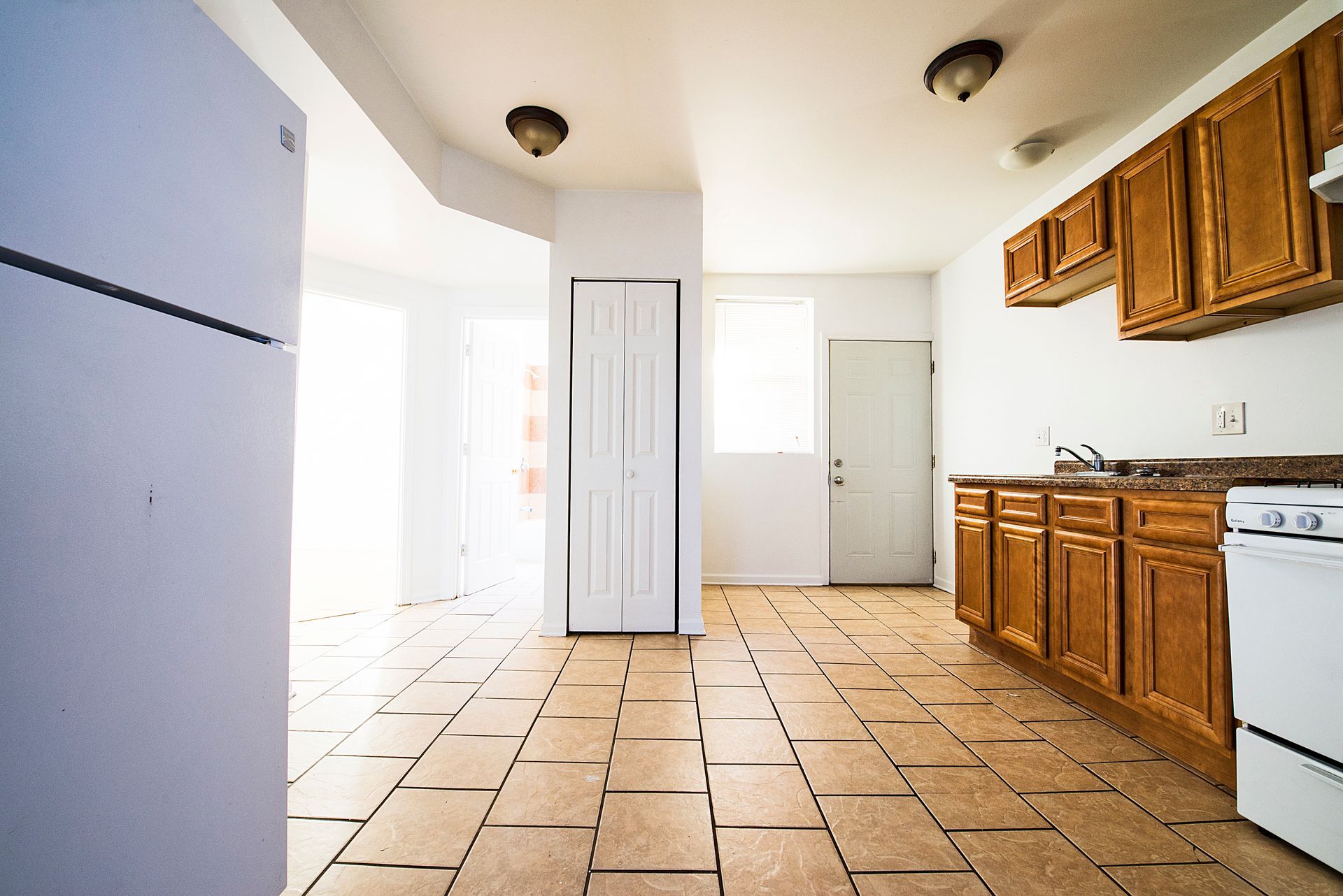 Empty kitchen with light brown cabinets, white appliances, and tiled floor.