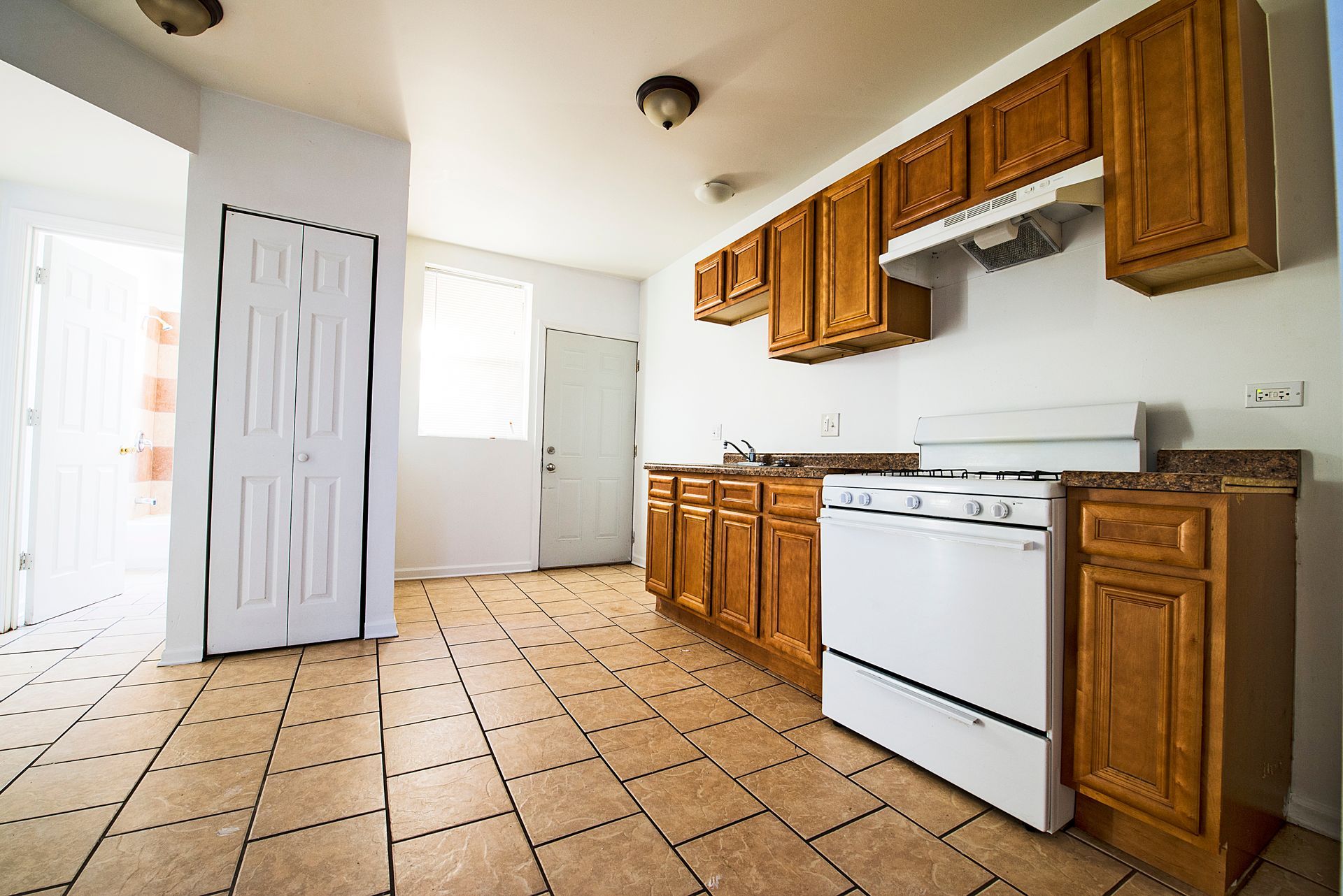 Kitchen with wooden cabinets, white appliances, and tiled floor. A doorway leads to another room.