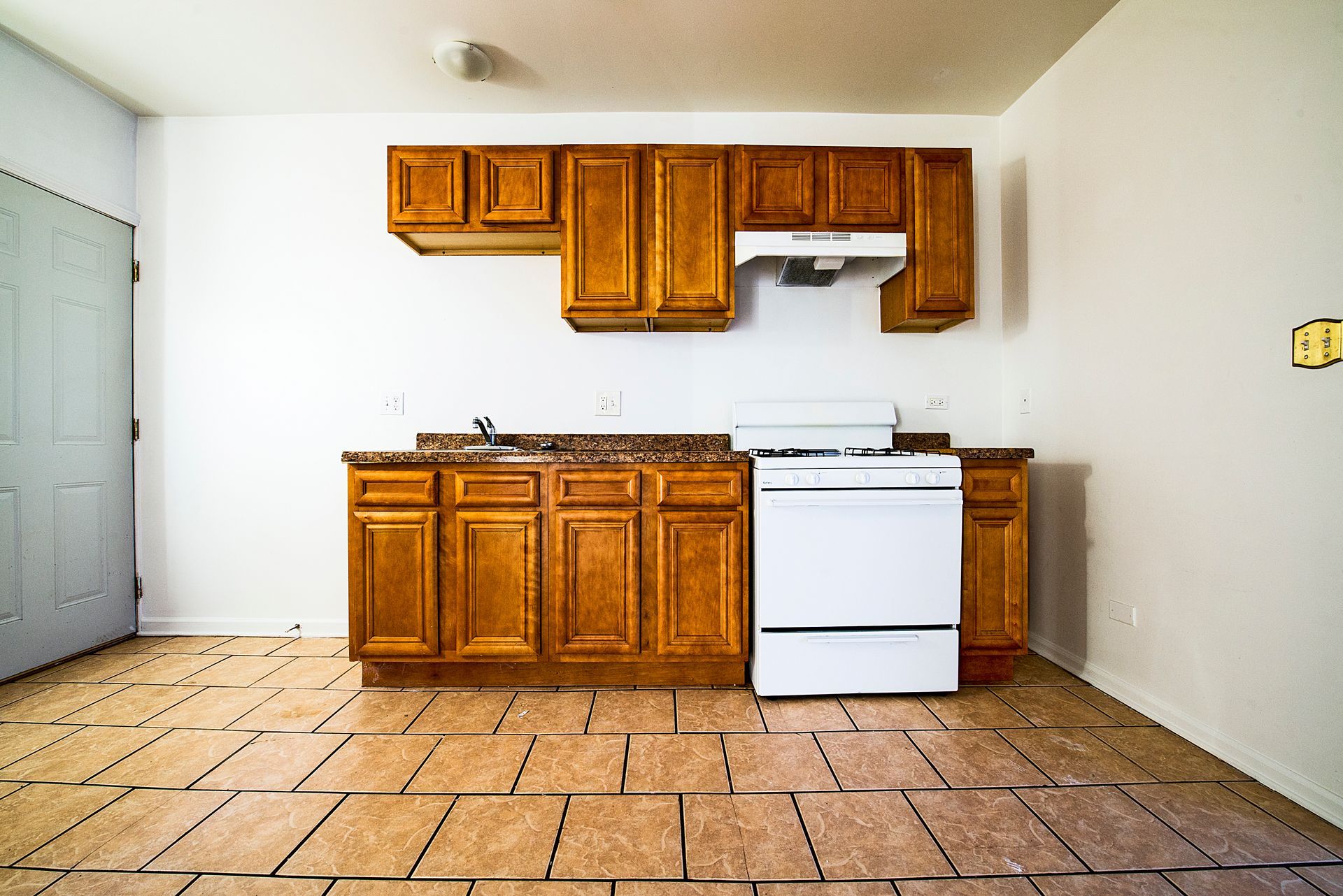 Empty kitchen with brown cabinets, white stove, and tiled floor.