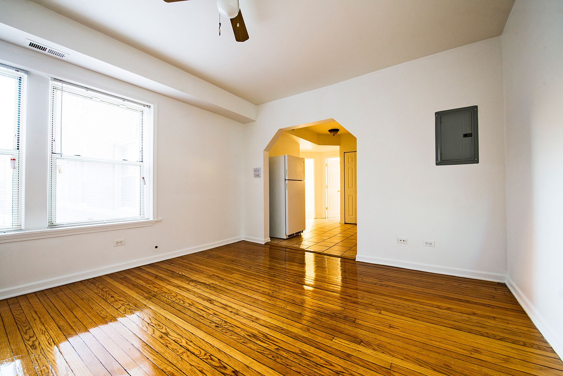 Empty room with hardwood floors, two windows, and an arched doorway leading to another room.