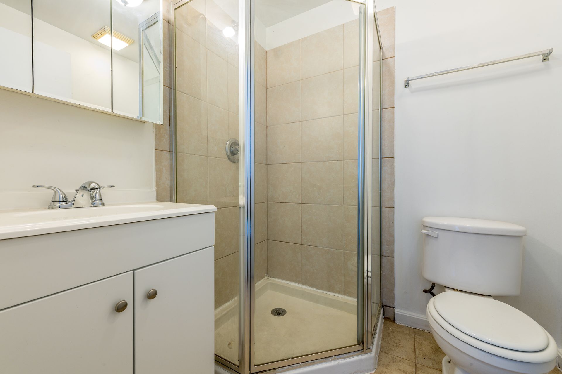 Small bathroom with shower, vanity, and toilet. Light-colored tiles and walls.