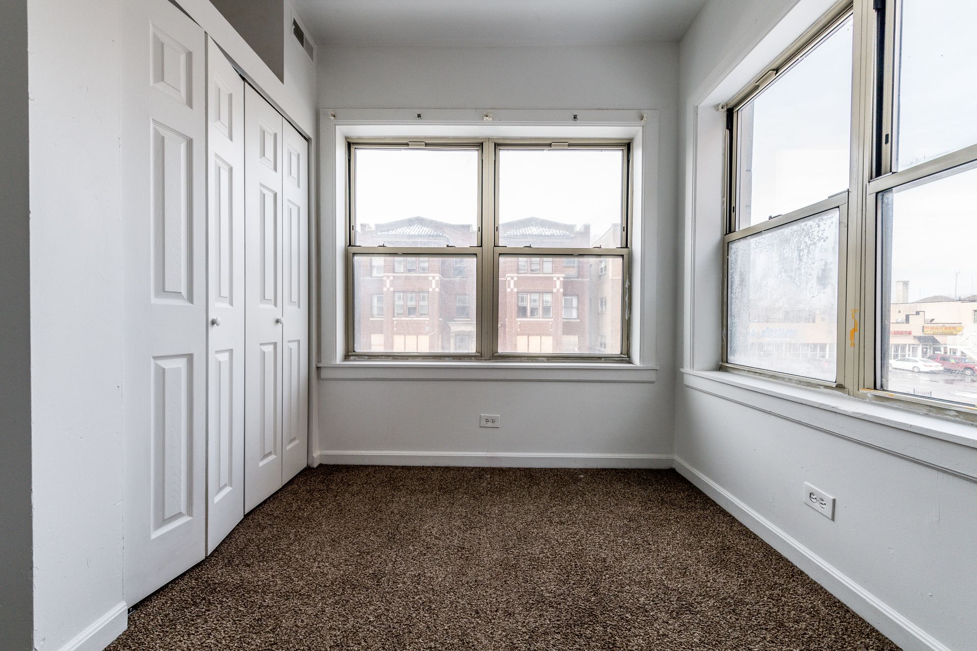 Empty room with white walls, carpet, windows, and a closet.
