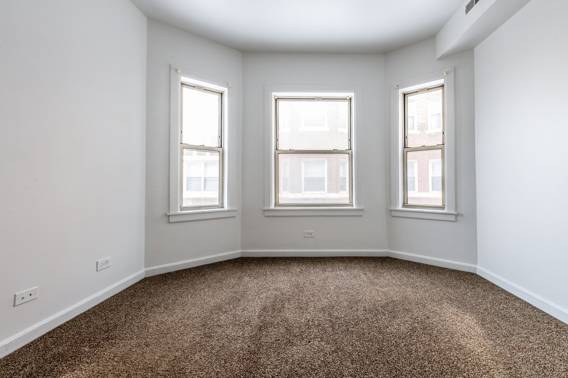 Empty room with bay windows, brown carpet, and white walls.