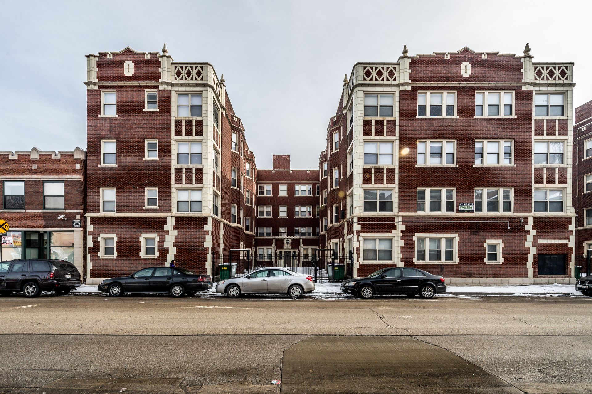 Brick apartment buildings with cars parked along the street on a cloudy day.