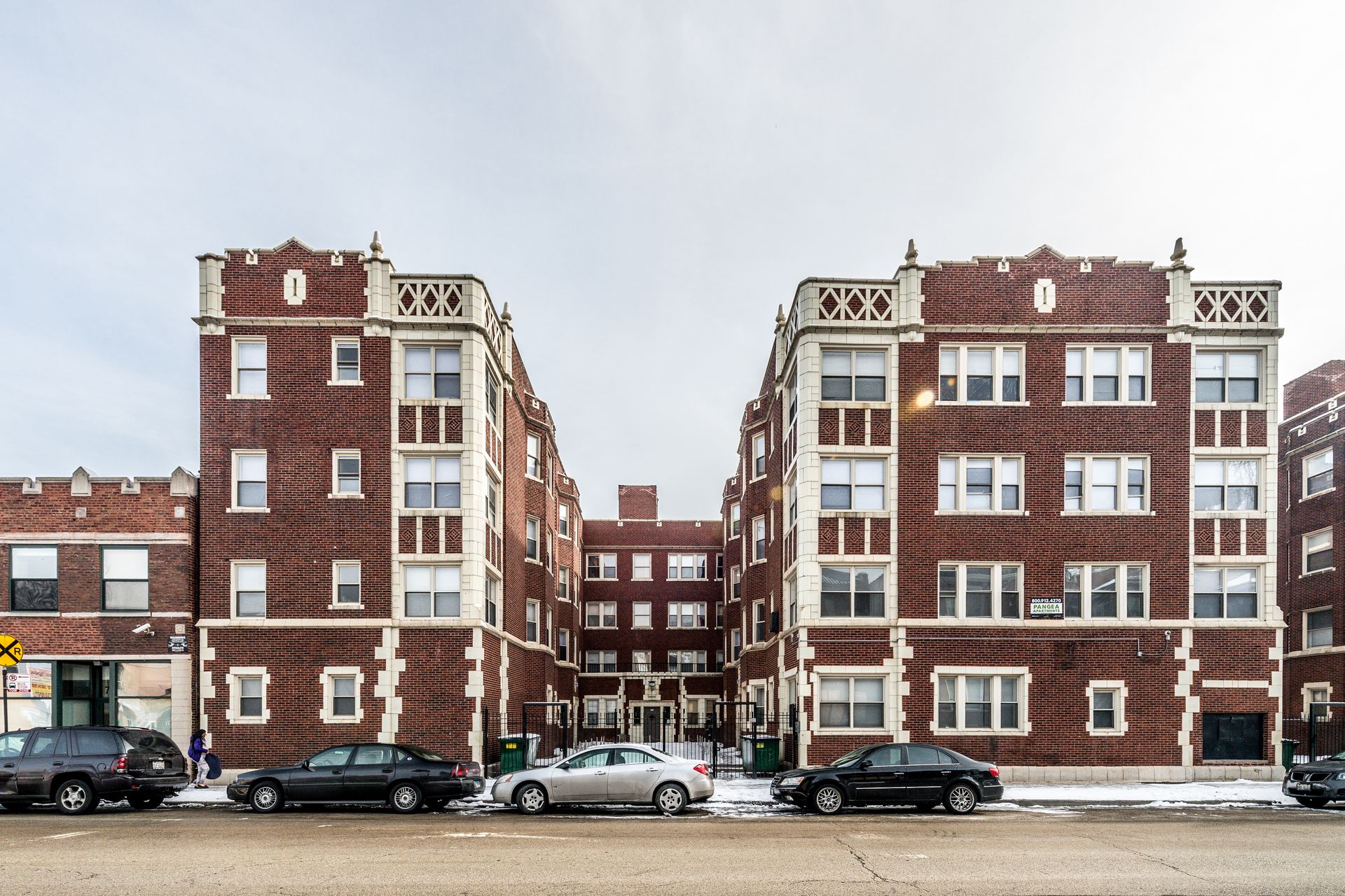 Multi-story brick apartment buildings with decorative trim on a snowy day. Cars parked along street.
