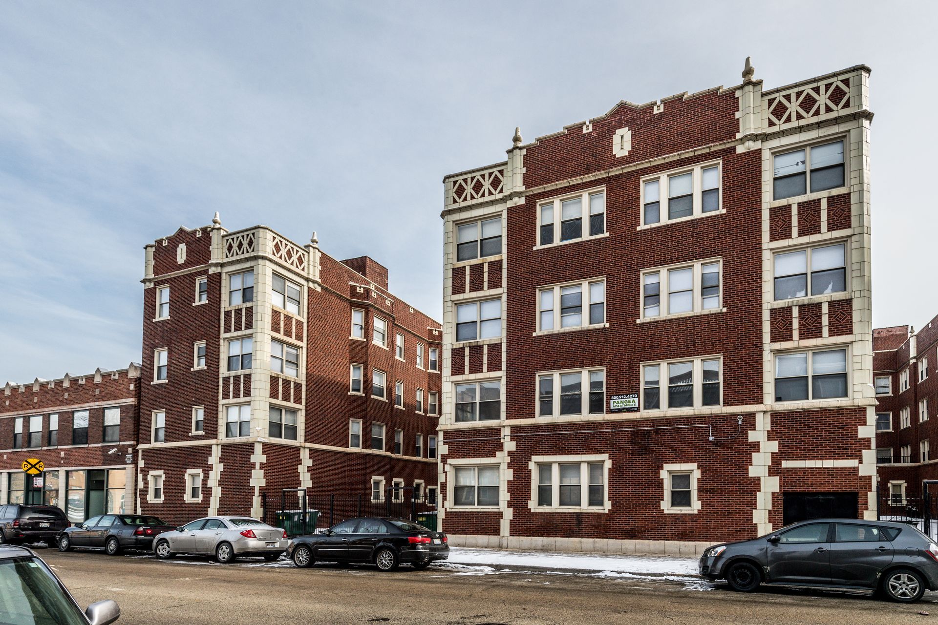 Multi-story brick apartment buildings with decorative trim; cars parked on street.