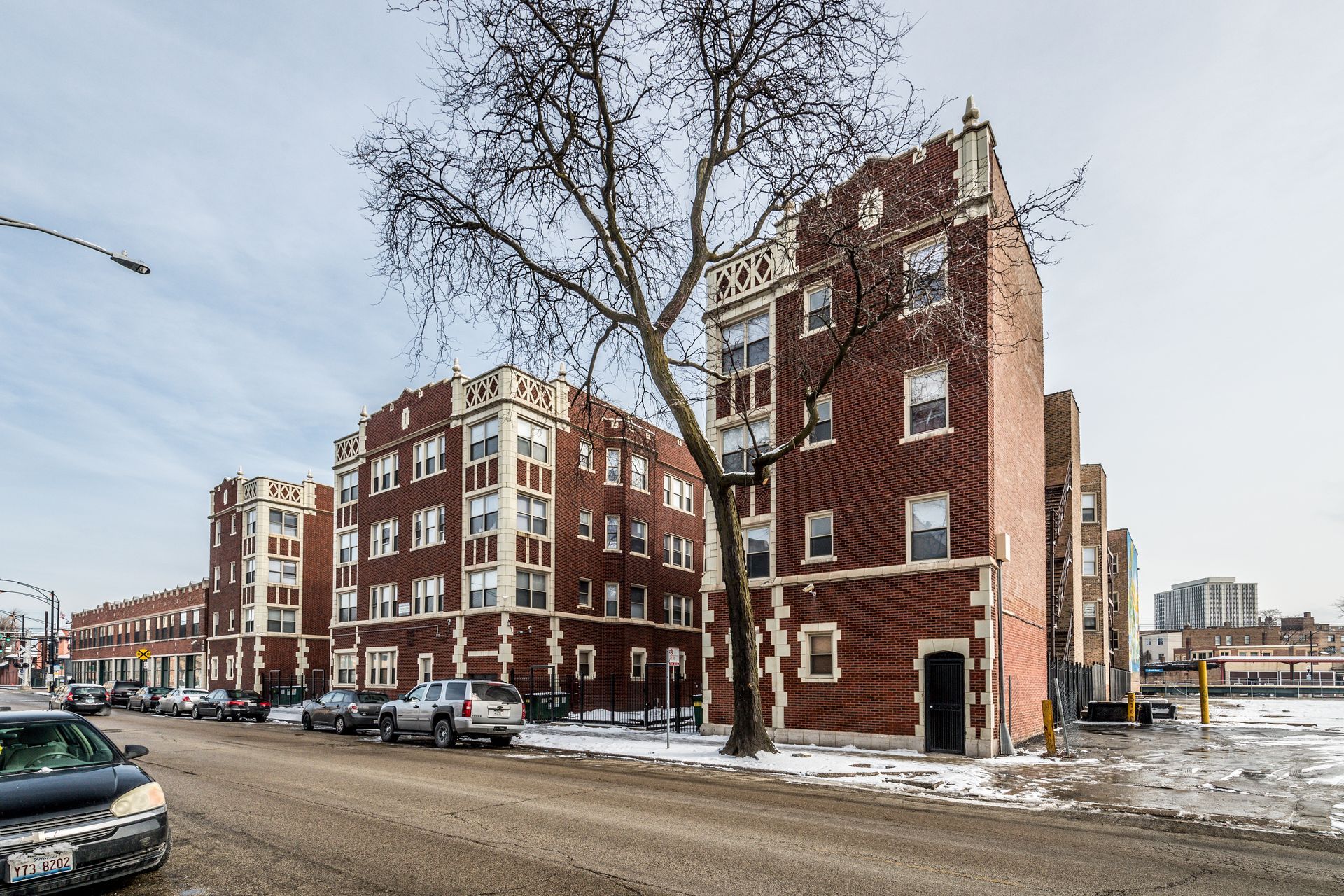 Red brick apartment buildings on a city street in winter; cars parked along the curb.