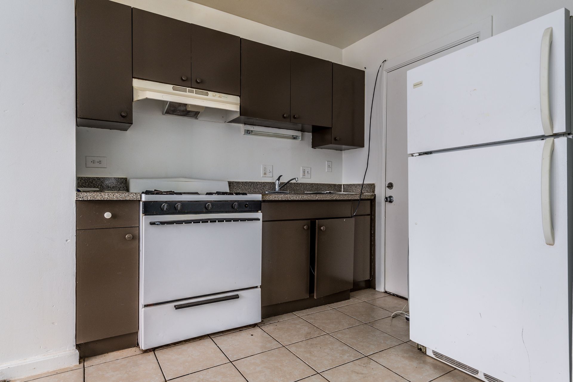 Kitchen with brown cabinets, white stove and fridge, granite countertop, and tile floor.