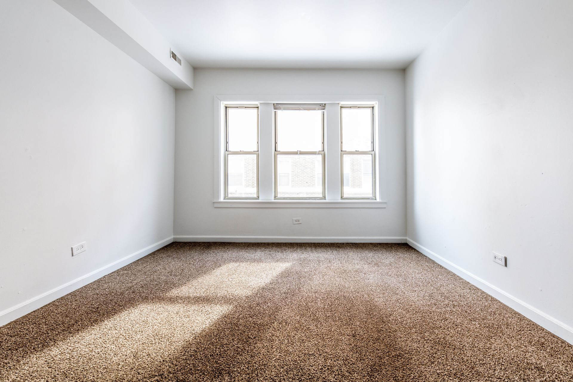 Empty room with three-paneled window. Brown speckled carpet and white walls.