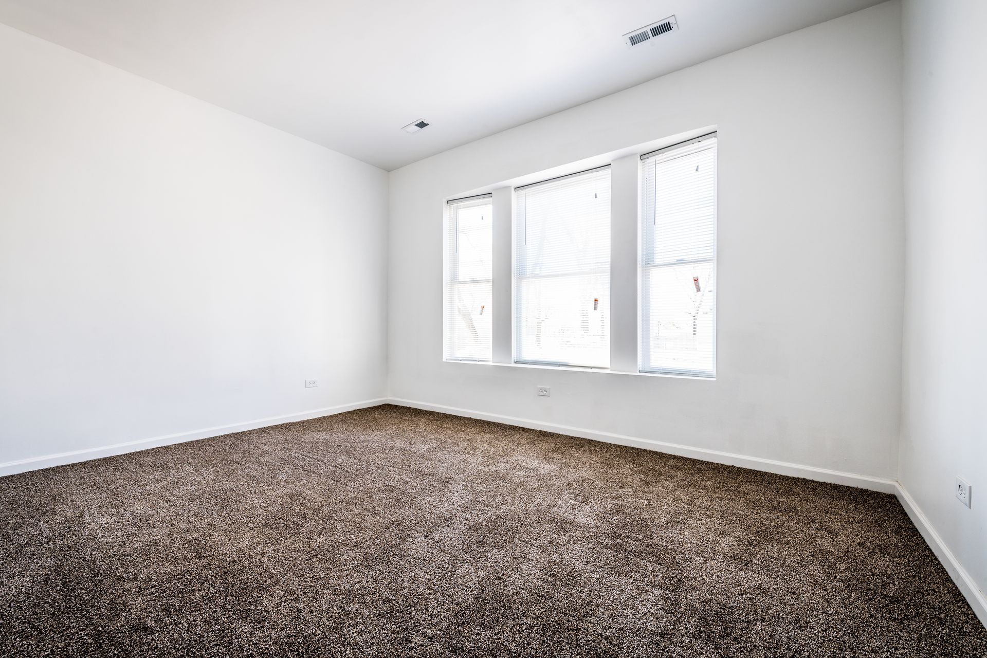 Empty room with brown carpet, white walls, and a triple window with blinds.