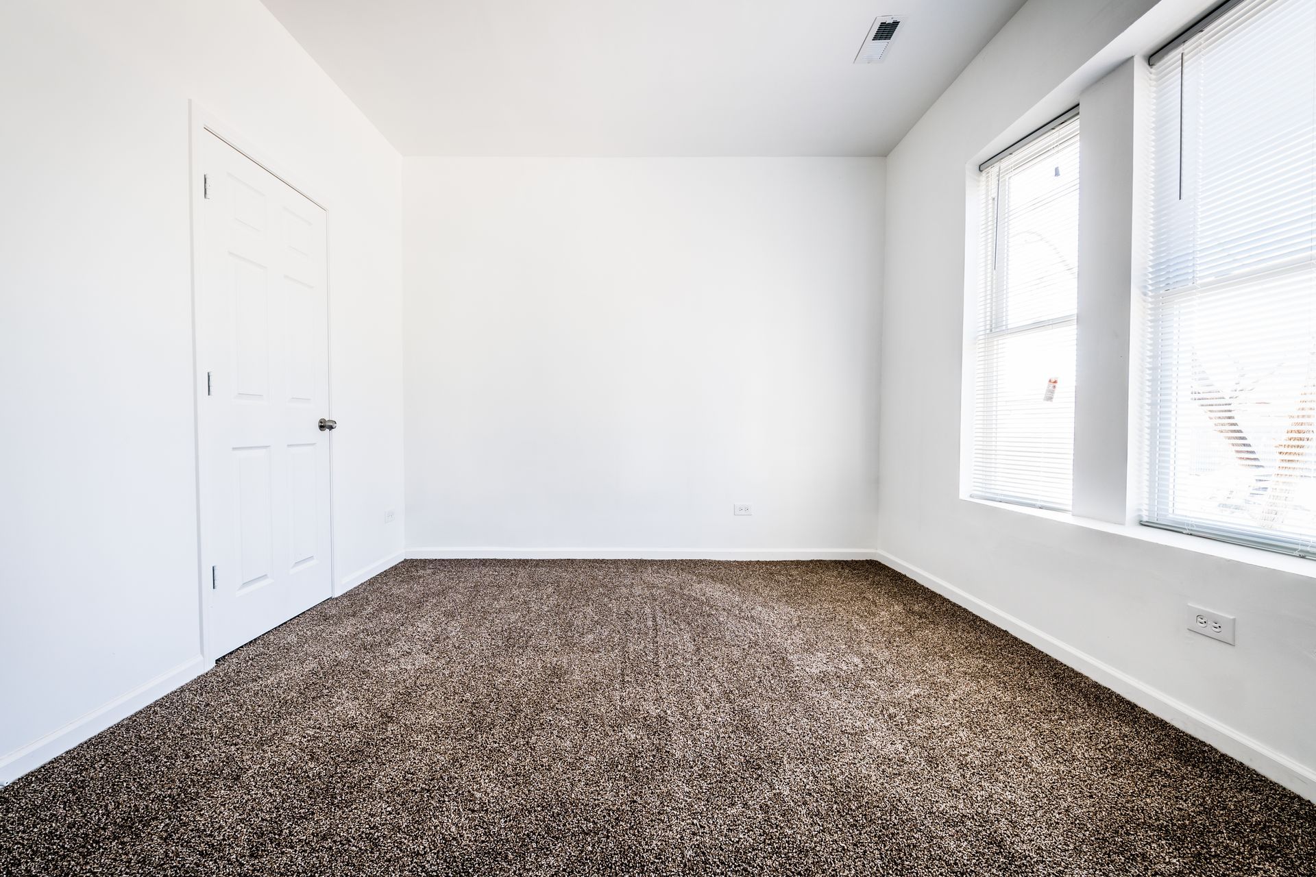 Empty room with brown carpet, white walls, door, and windows with blinds.