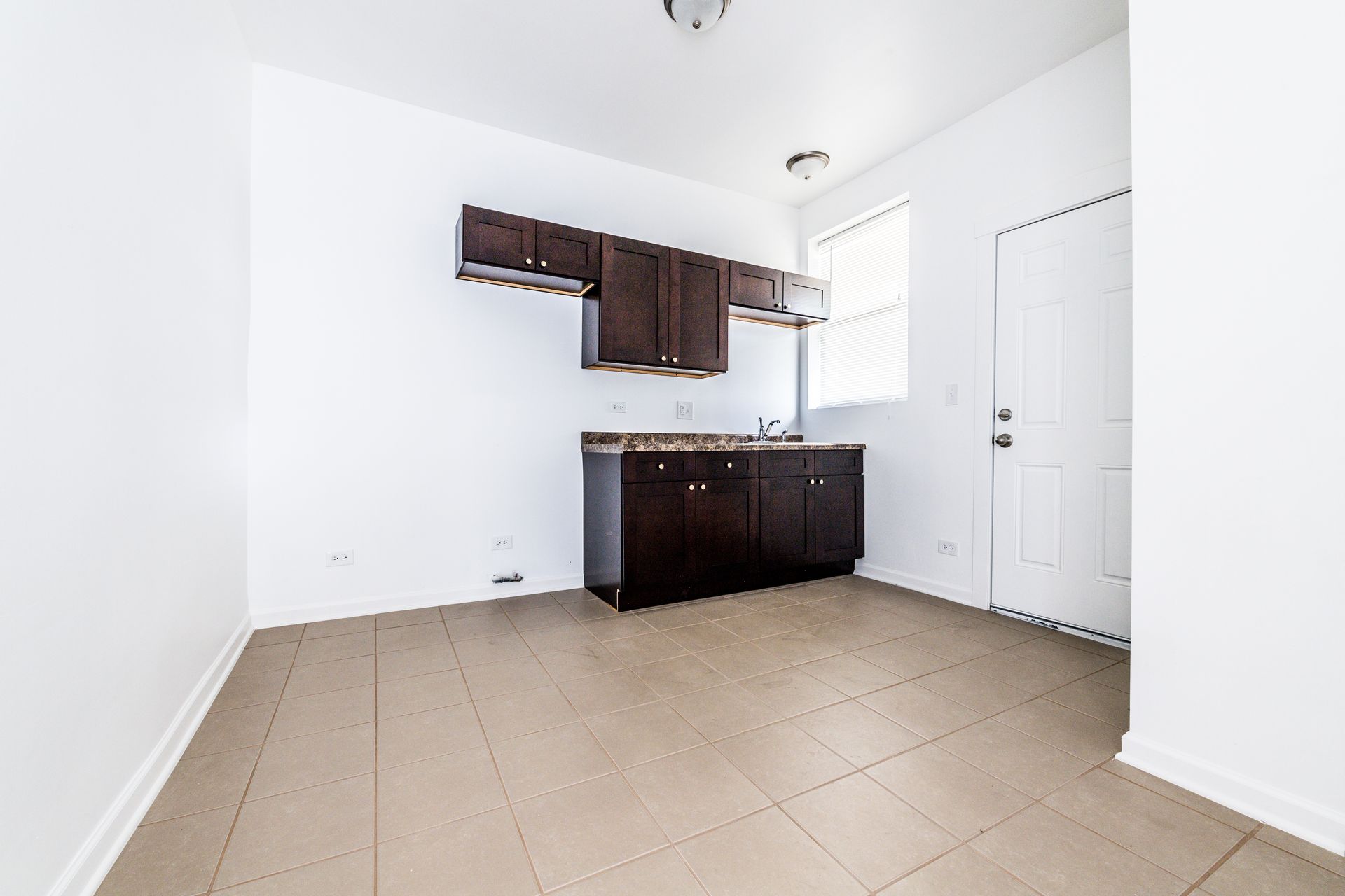 Empty kitchen with dark brown cabinets, tile floor, and white walls.
