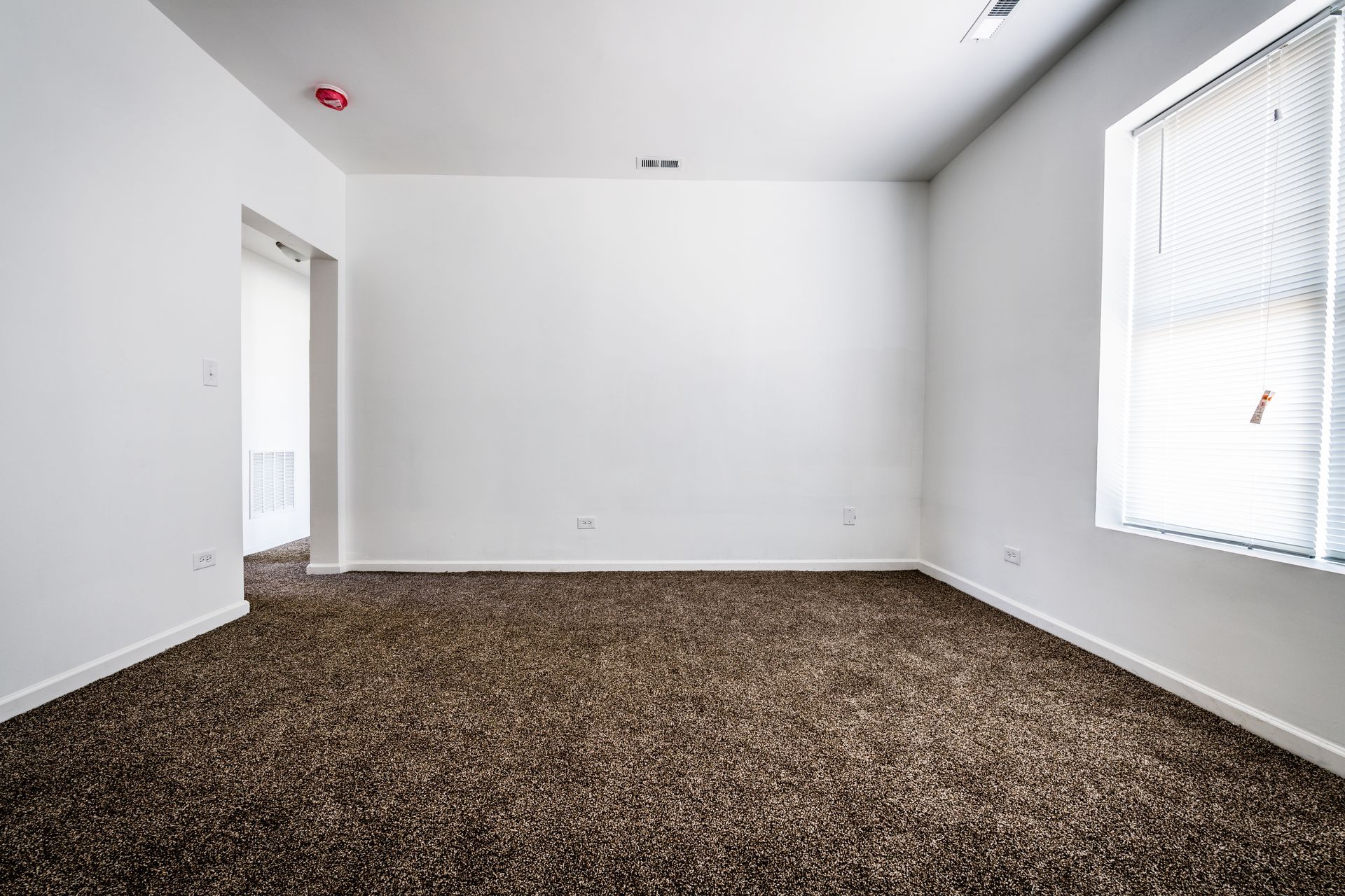 Empty room with brown carpet, white walls, and a window with blinds.