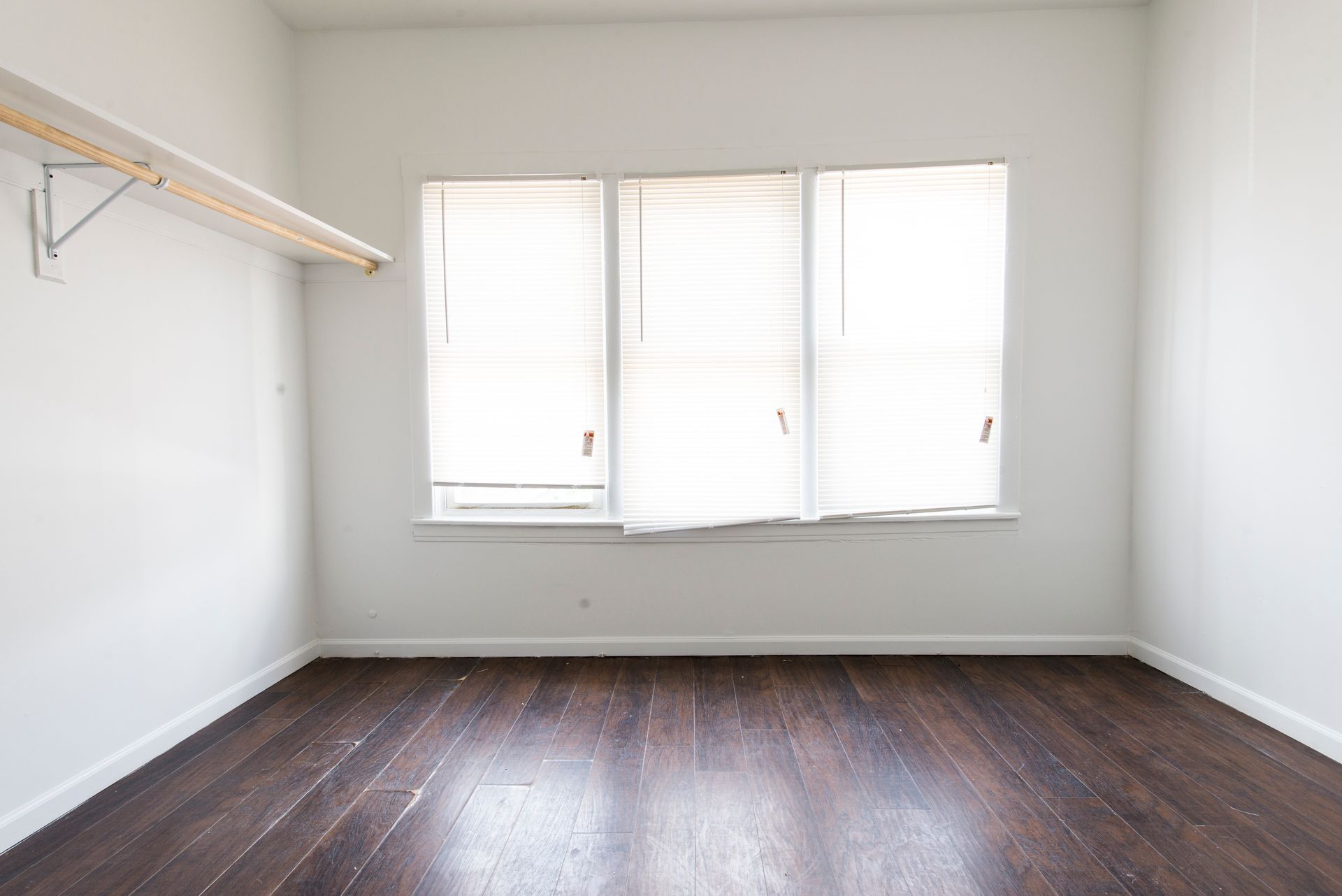 Empty room with dark hardwood floor, three windows, and a closet rod.