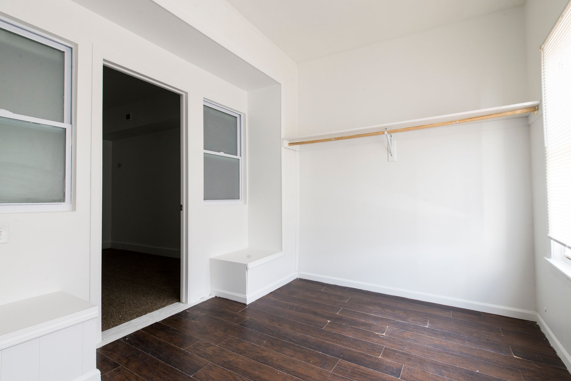 Empty room with dark wood floors, white walls, closet rod, and windows.