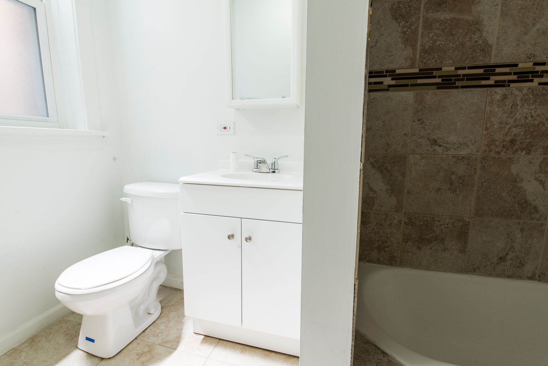 White bathroom with toilet, vanity, and shower/tub combo. Beige tile and neutral paint.
