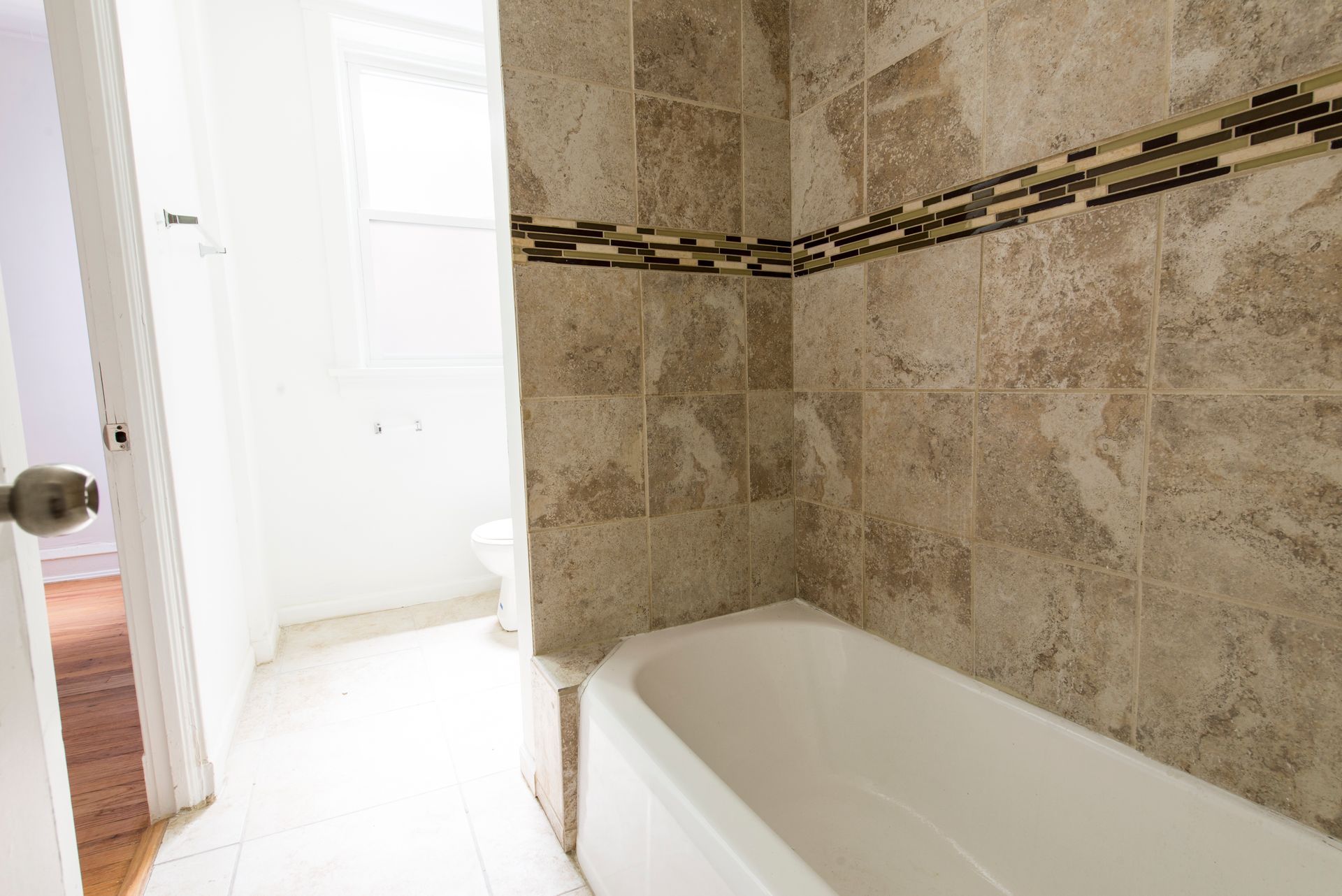 Bathroom with white tub, beige tiled walls, and small decorative tile band.