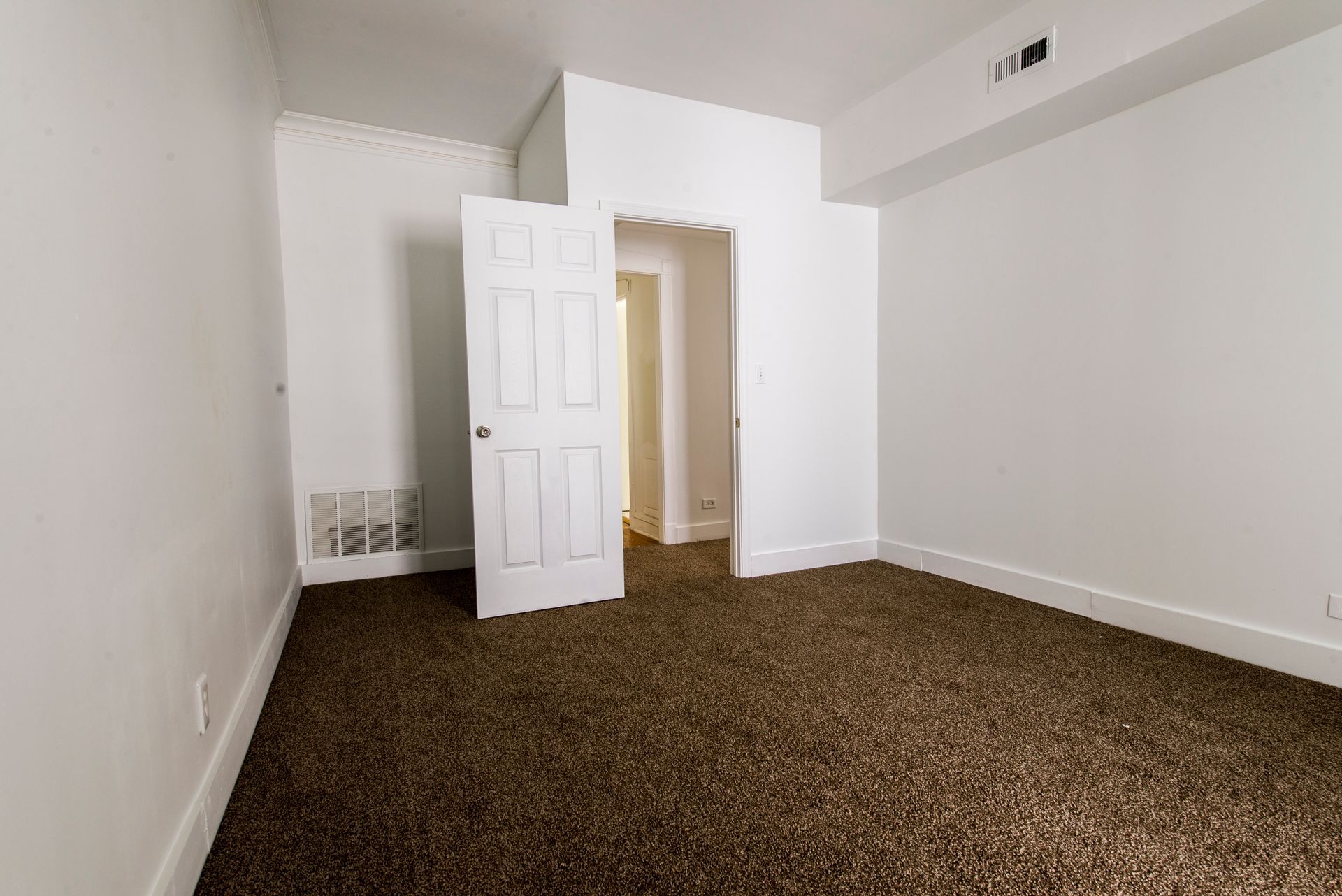 Empty room with brown carpet, white walls, and a partially open door to another room.