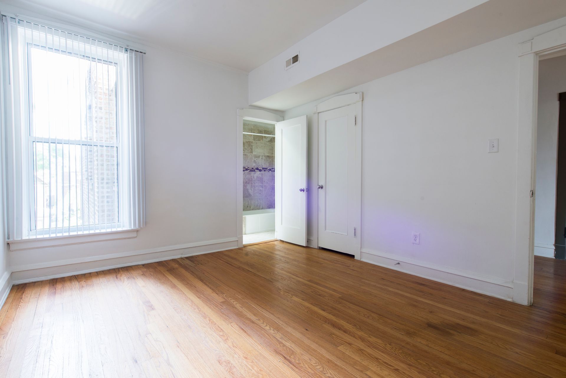 Empty room with hardwood floors, a window, and two doors. White walls and trim.