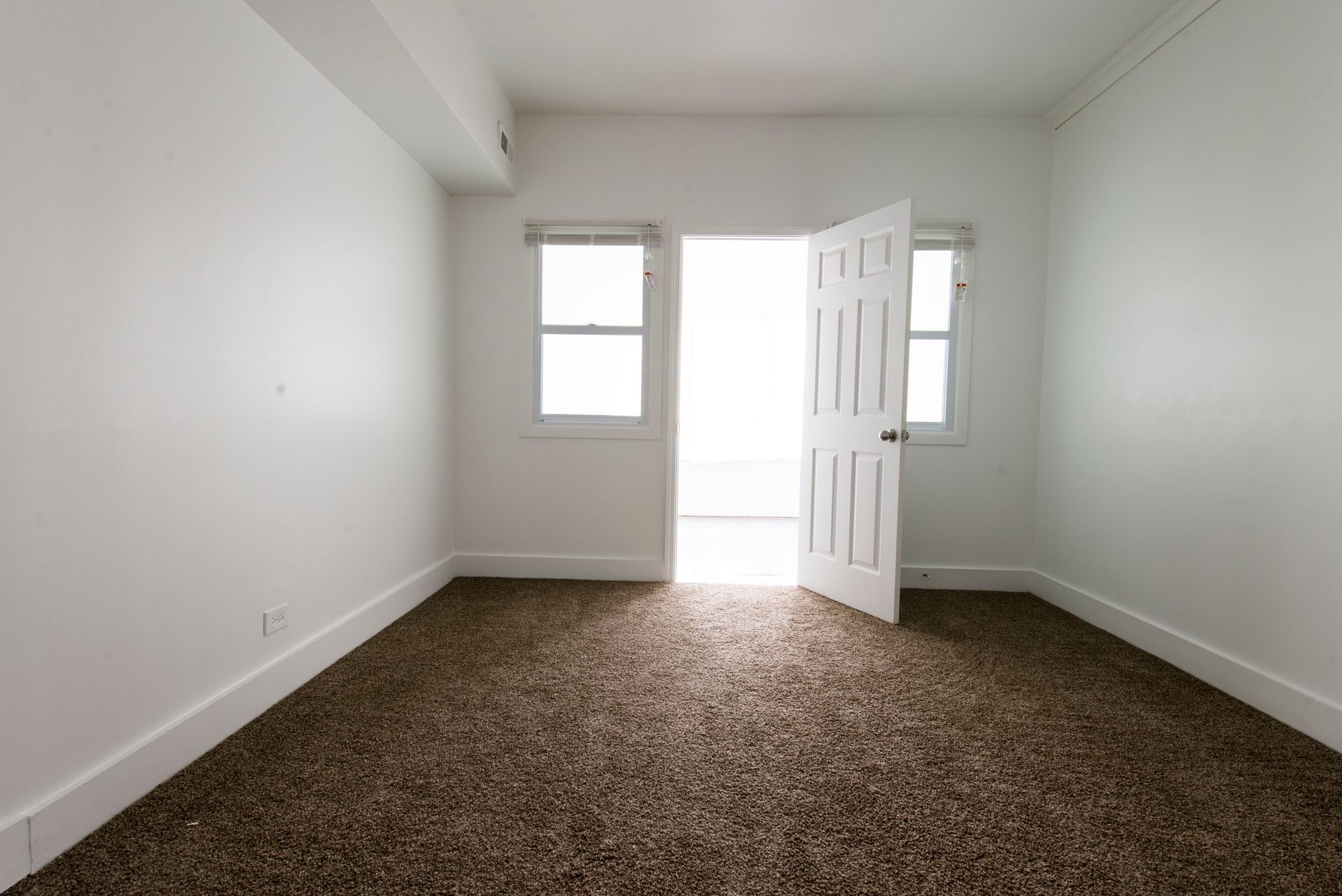 Empty room with brown carpet, two windows, and an open white door.