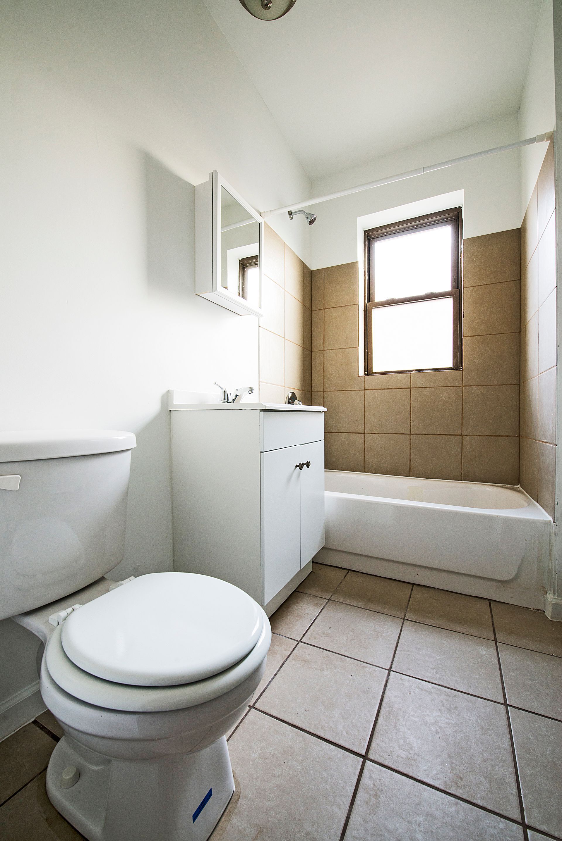 Bathroom with white toilet, sink, and bathtub; beige tiled walls and floor.
