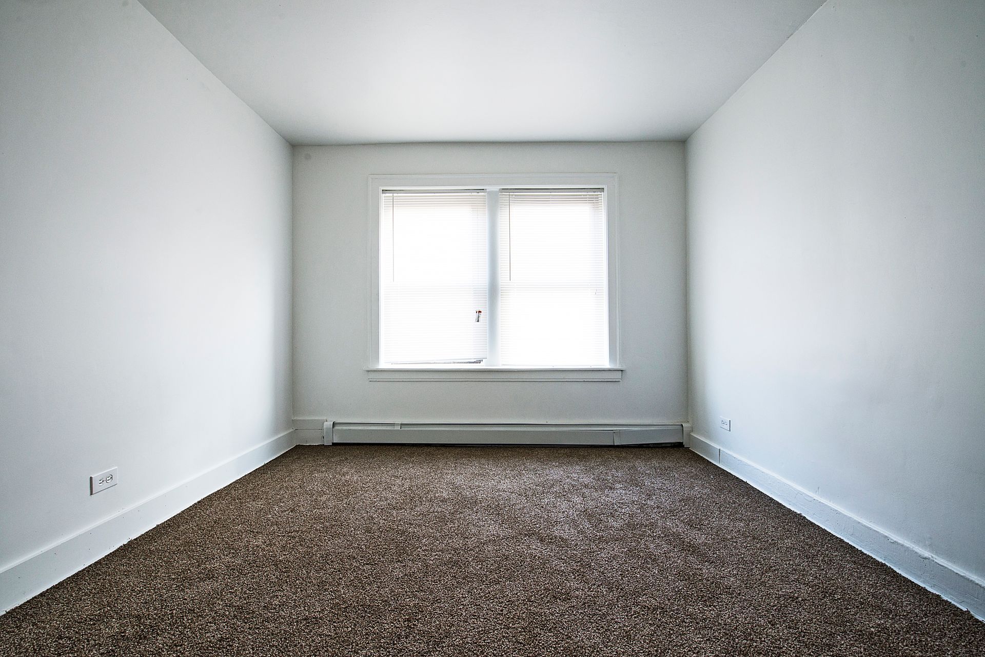 Empty room with white walls, window with blinds, and brown carpet.