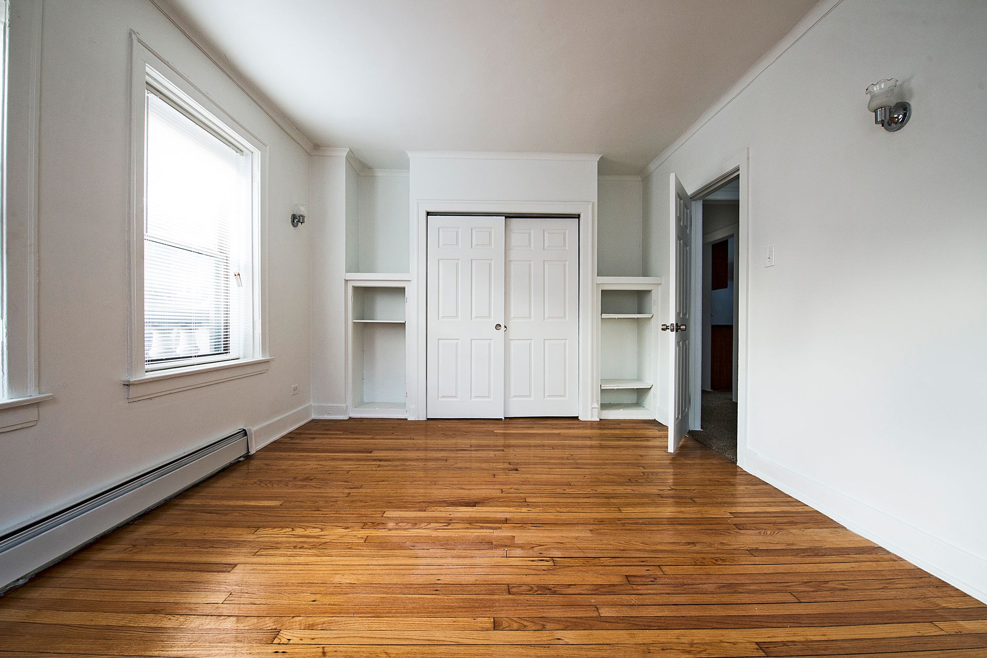 Empty room with hardwood floors, white walls, closet, built-in shelves, and a window.