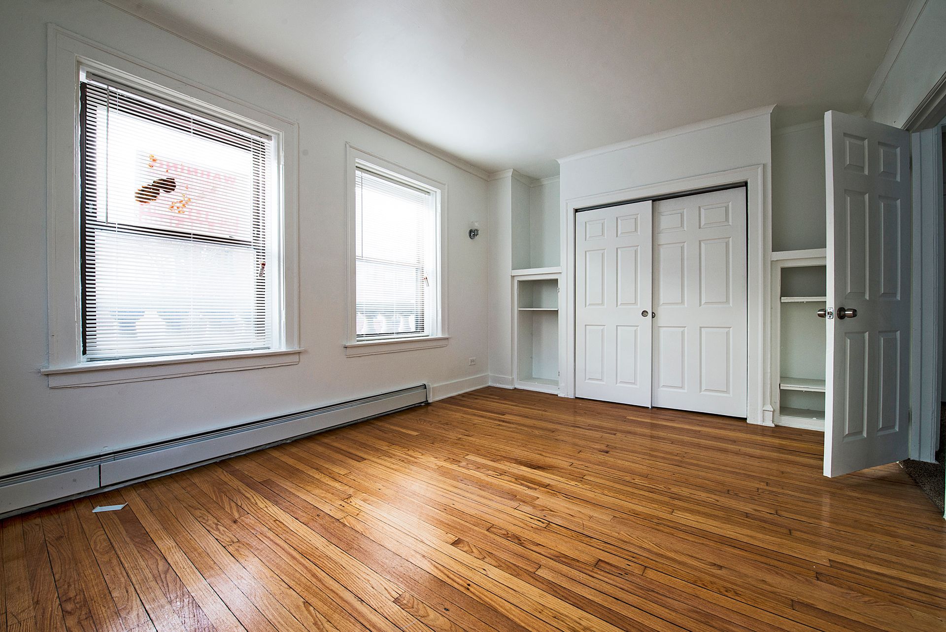 Empty room with wood floors, two windows, built-in closet, and open door.
