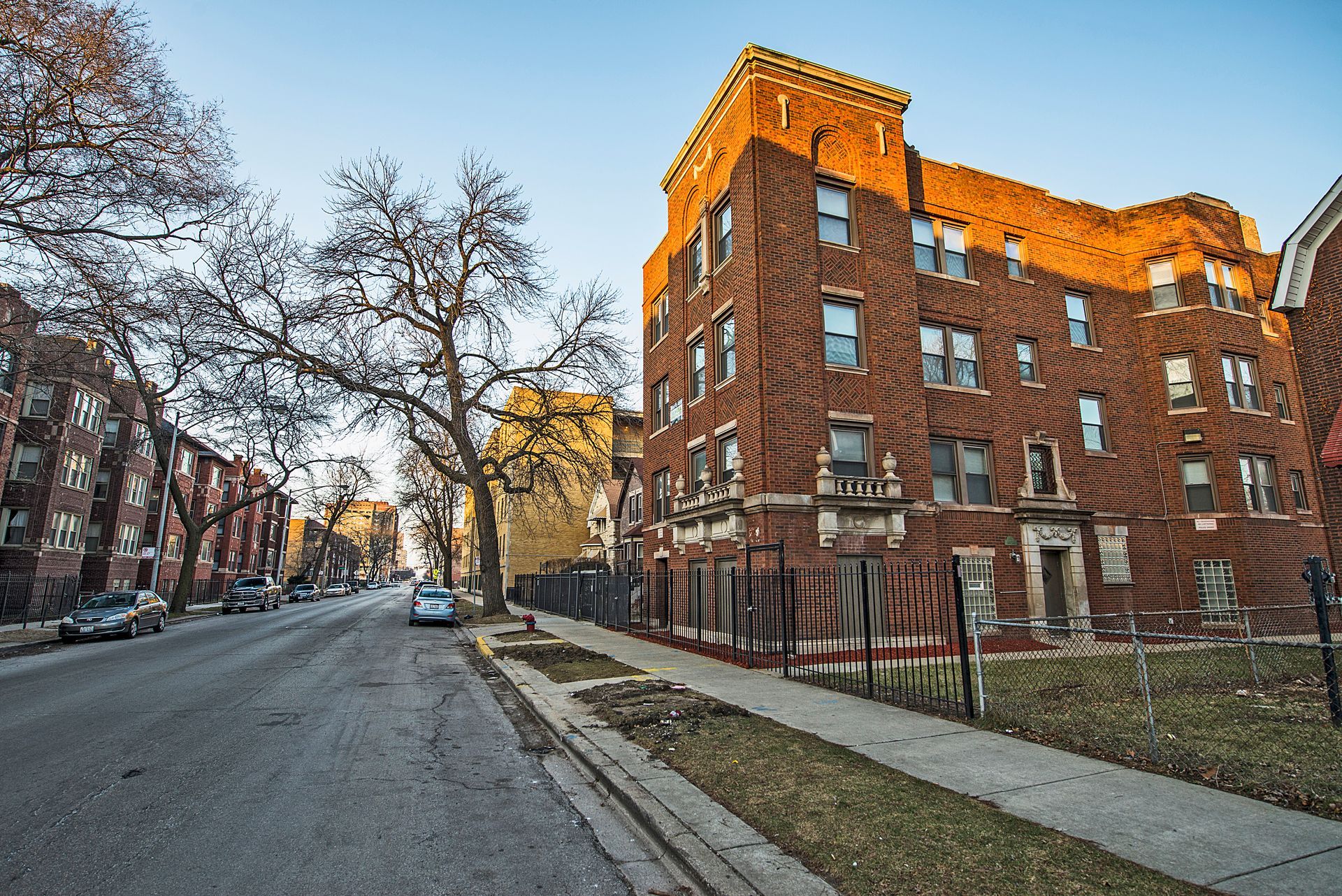 Street view of red brick apartment building bathed in sunlight.