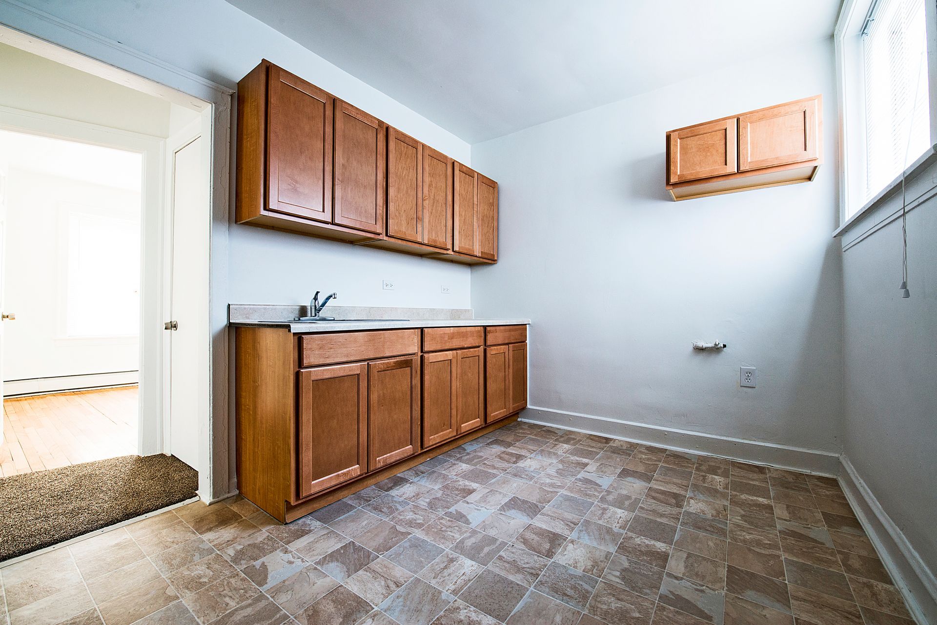 Empty kitchen with brown cabinets, sink, and linoleum floor. Doorway to left.