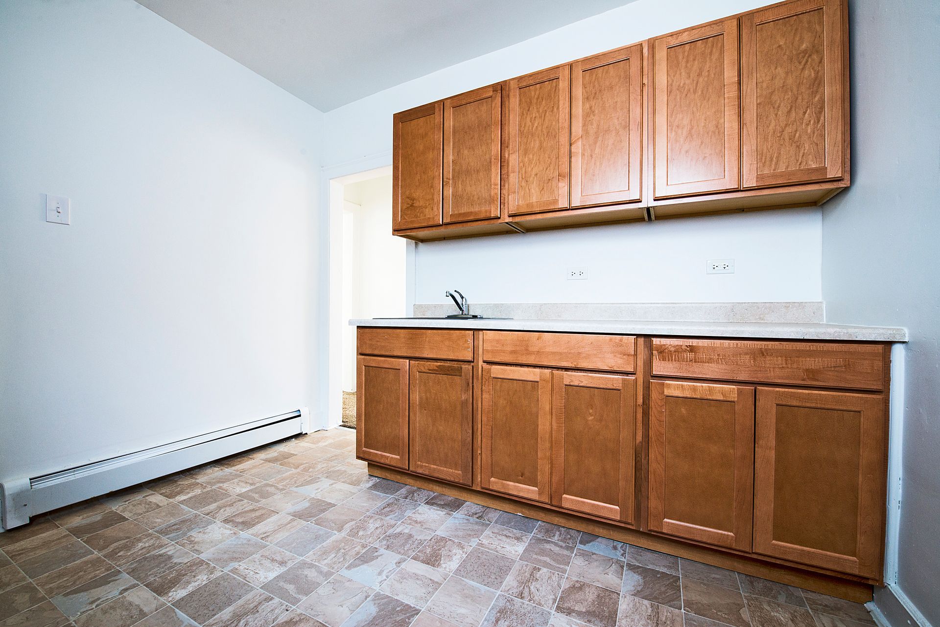 Empty kitchen with upper and lower wood cabinets, a sink, and beige tile floor.
