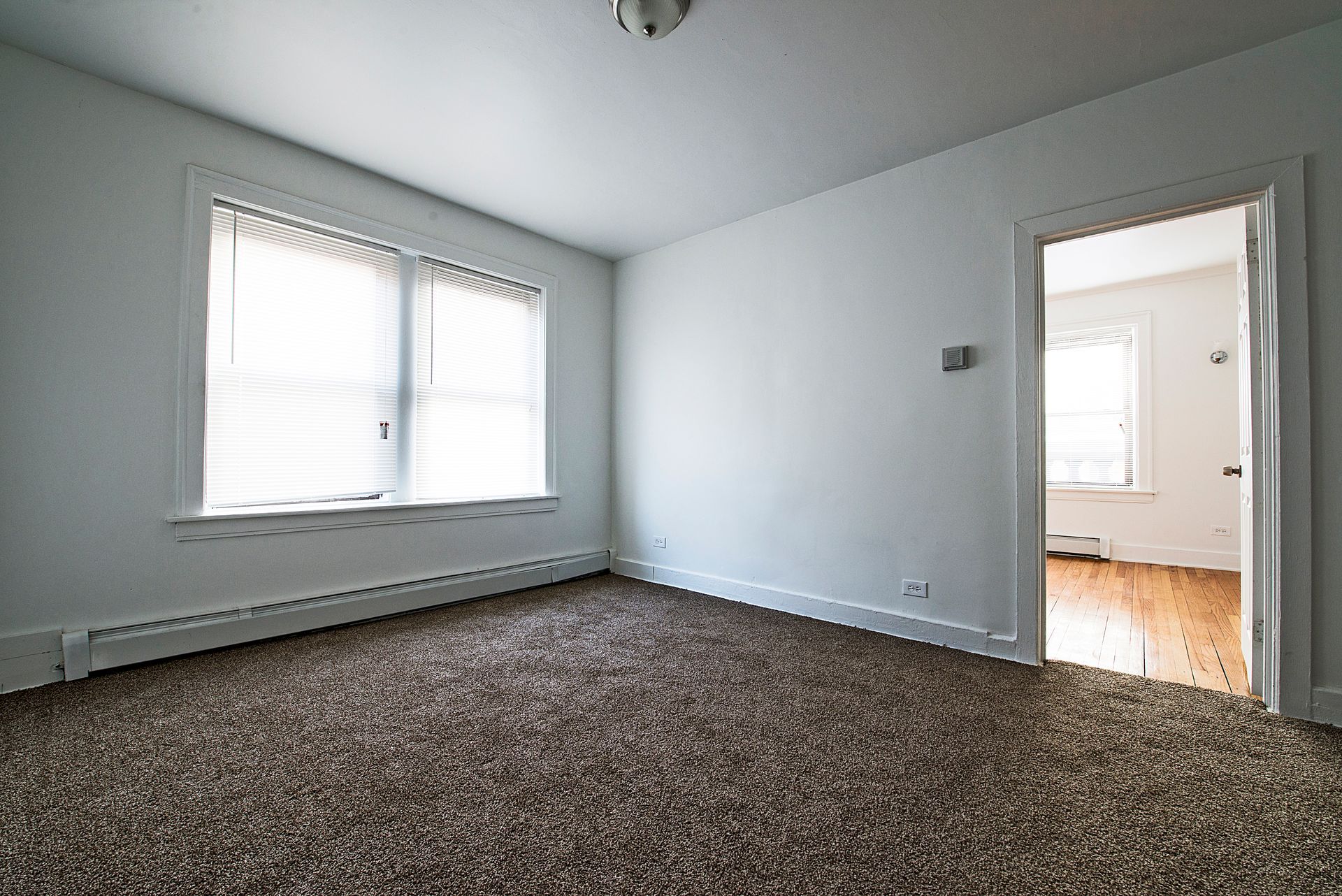 Empty room with brown carpet, white walls, and a doorway leading to another room.