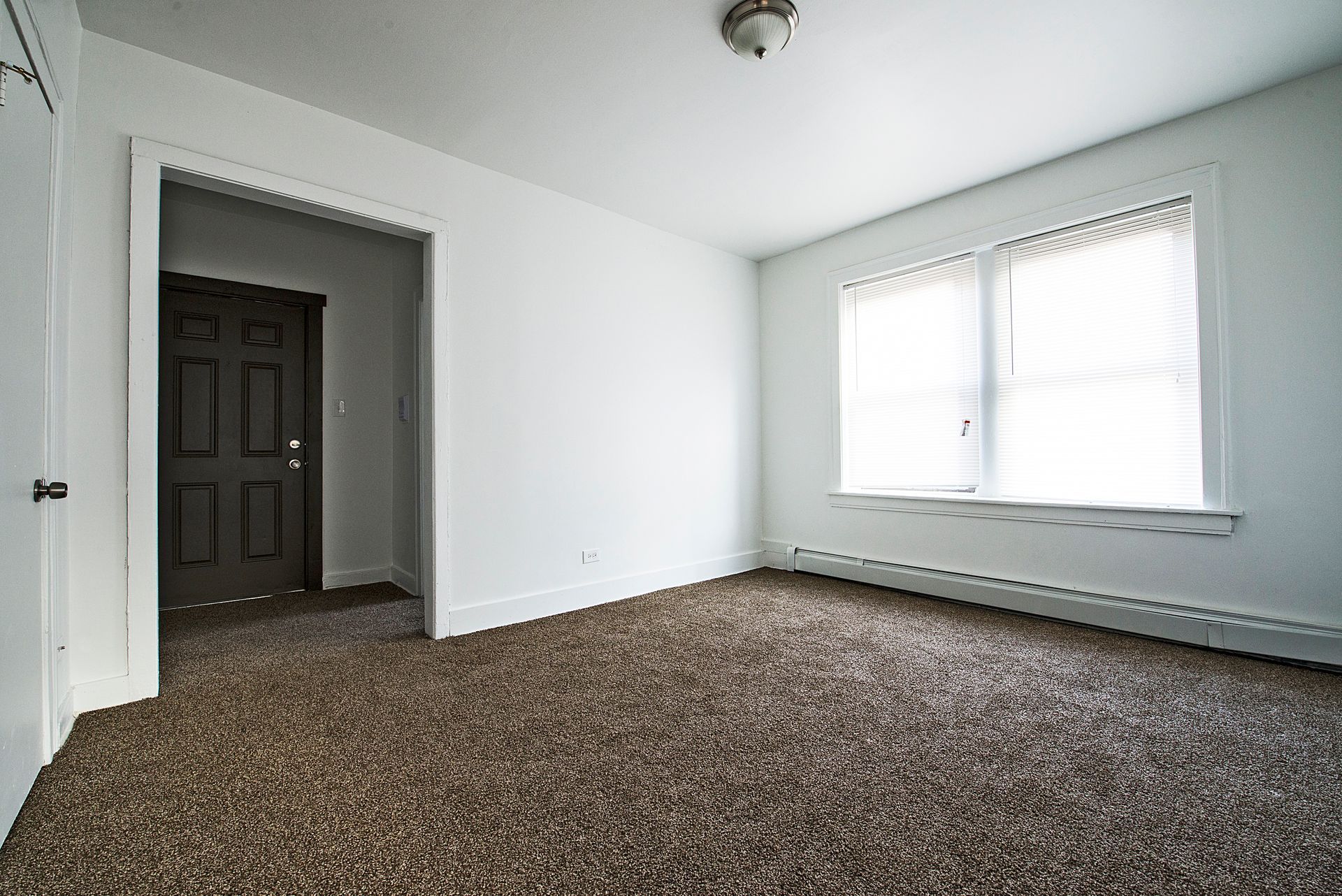Empty room with brown carpet, white walls, and a window. Doorway on the left.