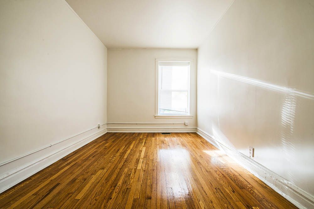 Empty room with hardwood floors, white walls, and a window.