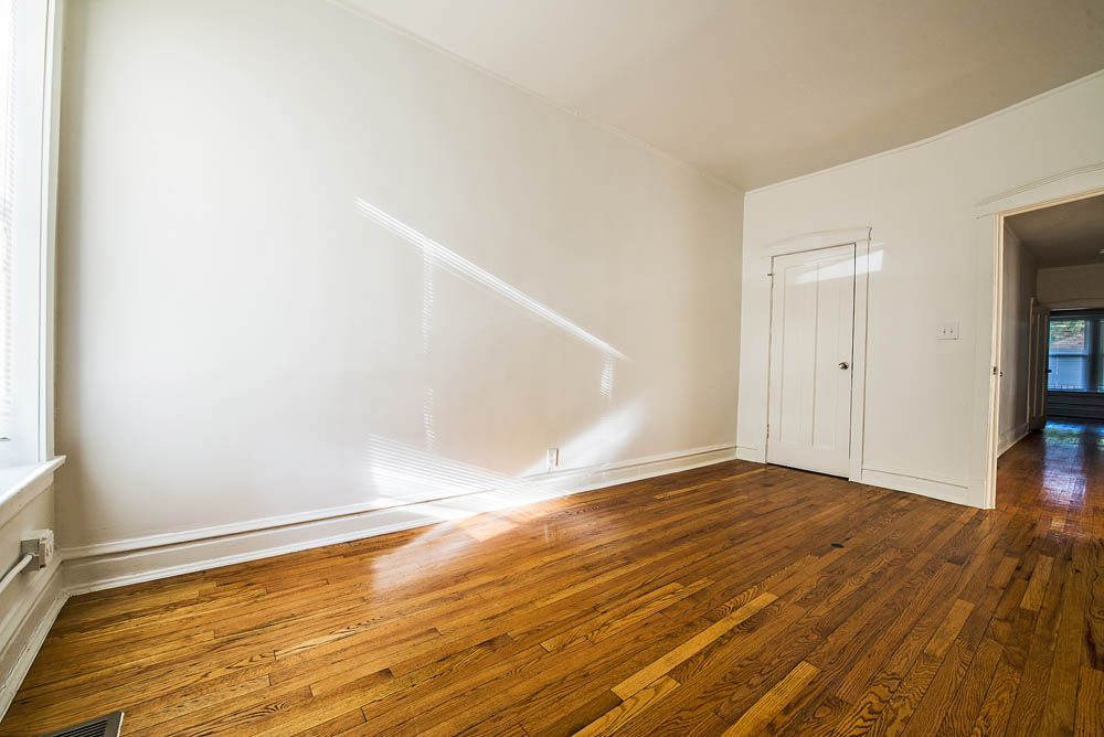 Empty room with hardwood floors, white walls, and a door opening to another room.