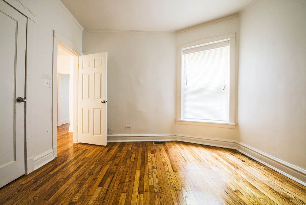 Empty room with wood floor, white walls, and a window with blinds. Doorways are open.