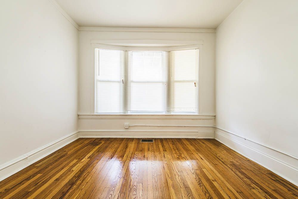 Empty room with hardwood floors, white walls, and a window with blinds.