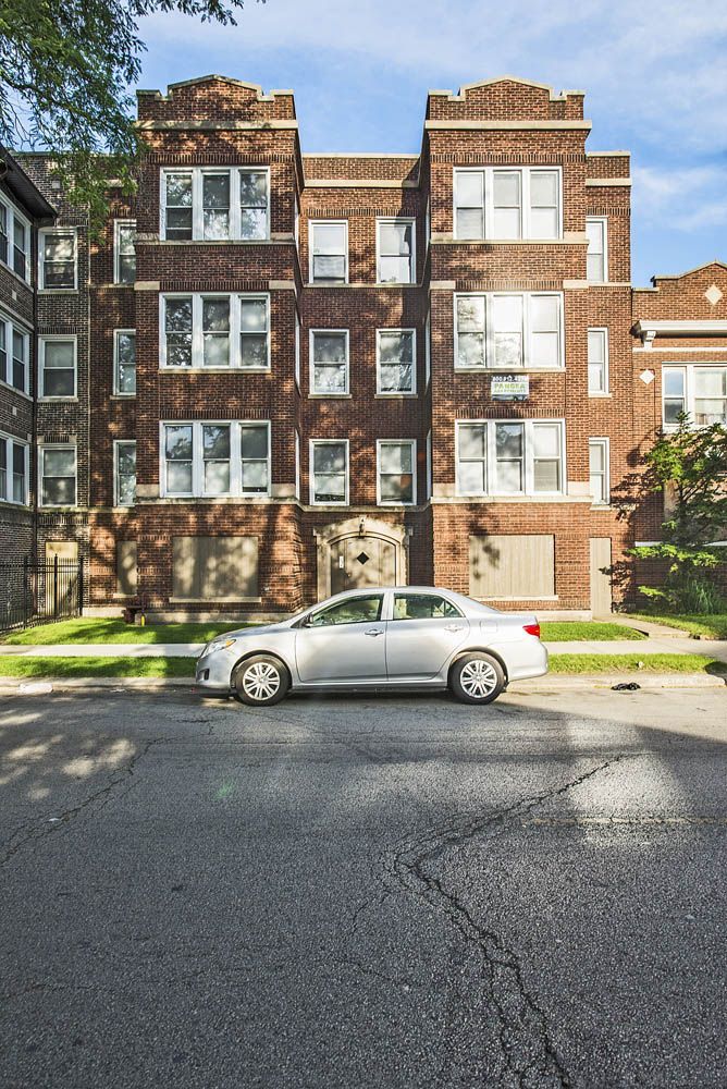 Silver sedan parked in front of a brick apartment building on a sunny day.