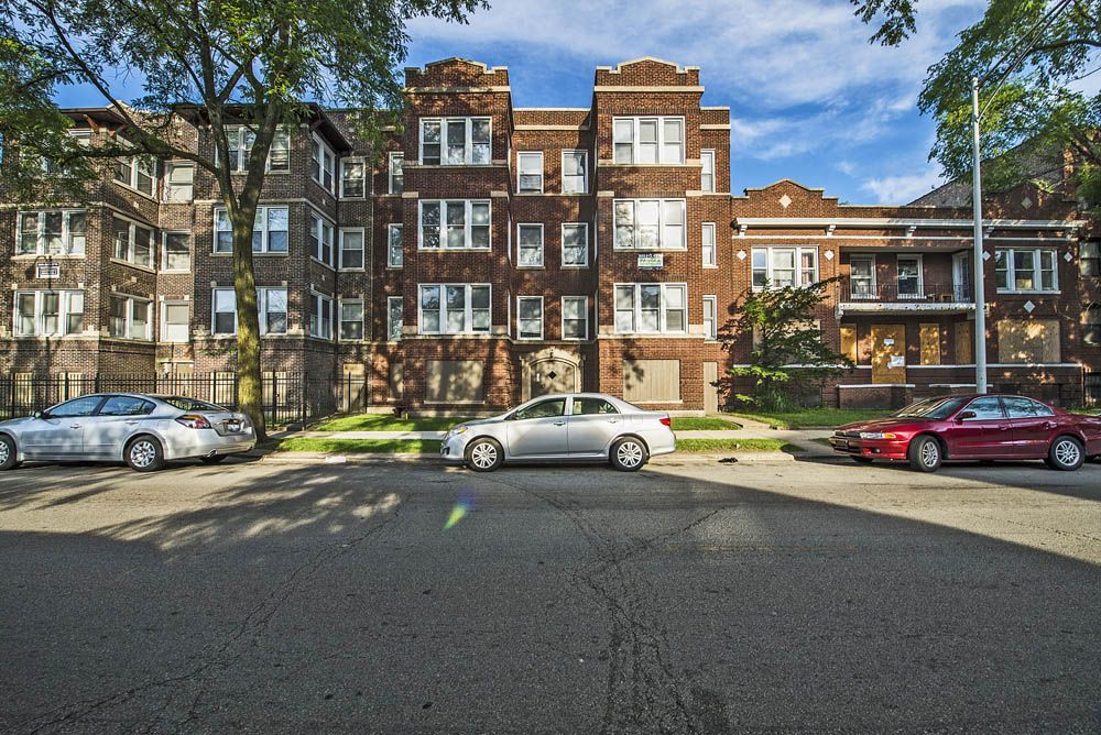Apartment building with cars parked on the street. Brown brick exterior, green lawn, blue sky.