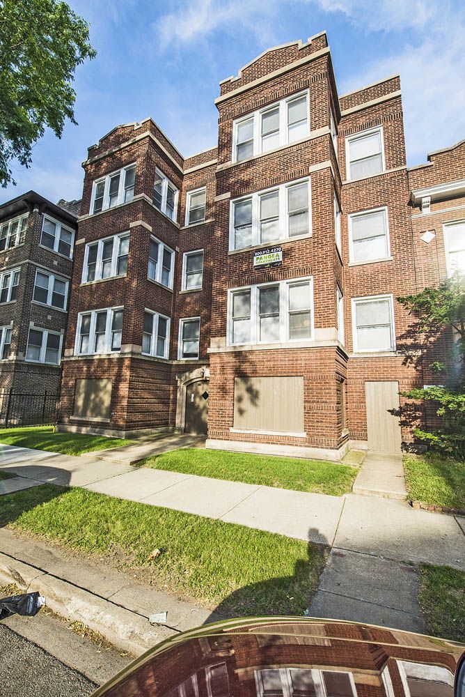 Multi-story brick apartment building with white-trimmed windows and green lawn.